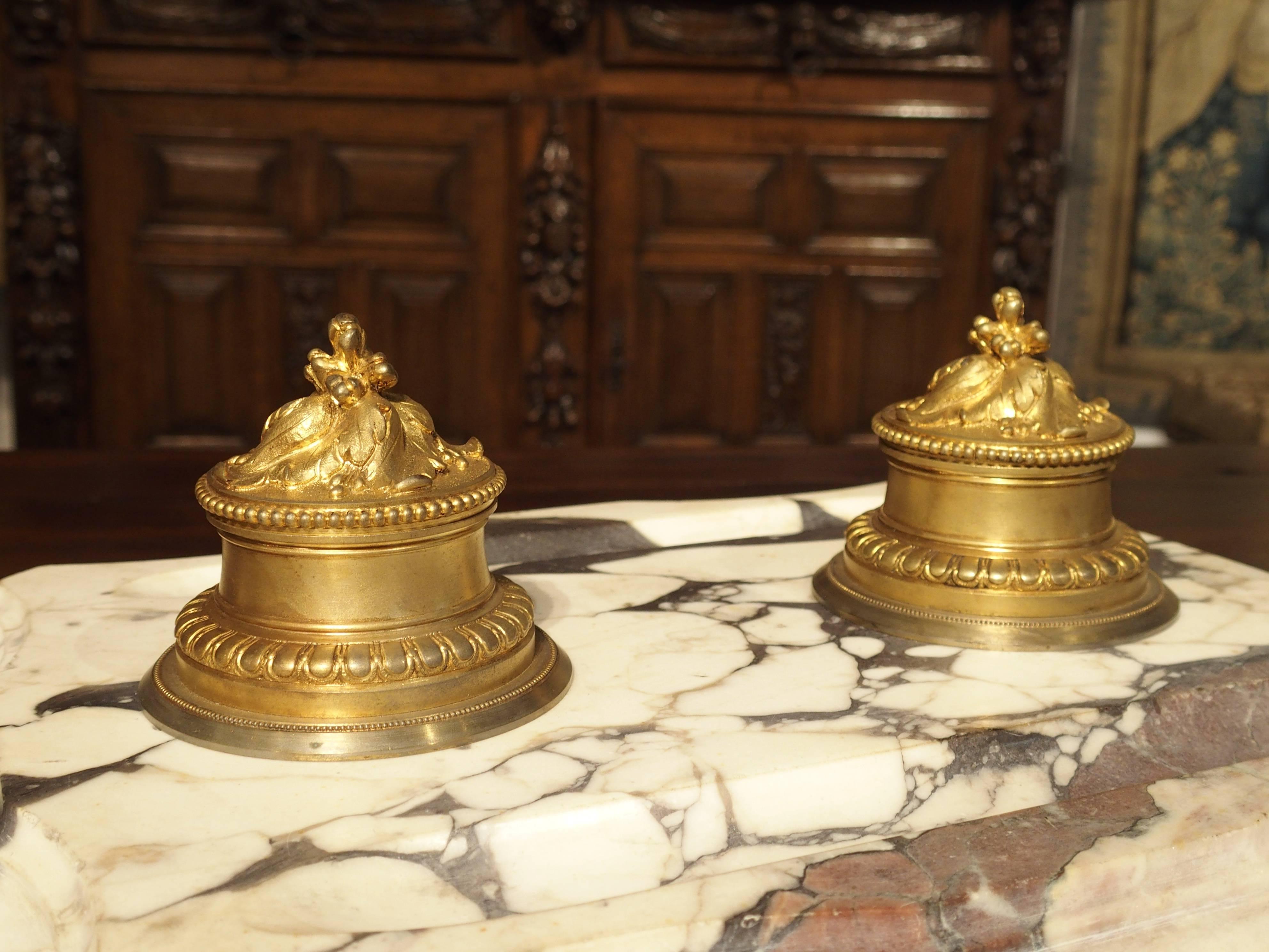 This is a stunning, large, antique French marble and gilt bronze double inkwell. The inkwells’ lids are hinged to the wells and have motifs of swirling leaves with berries culminating at the top for the pull. The other motifs are varying sizes of