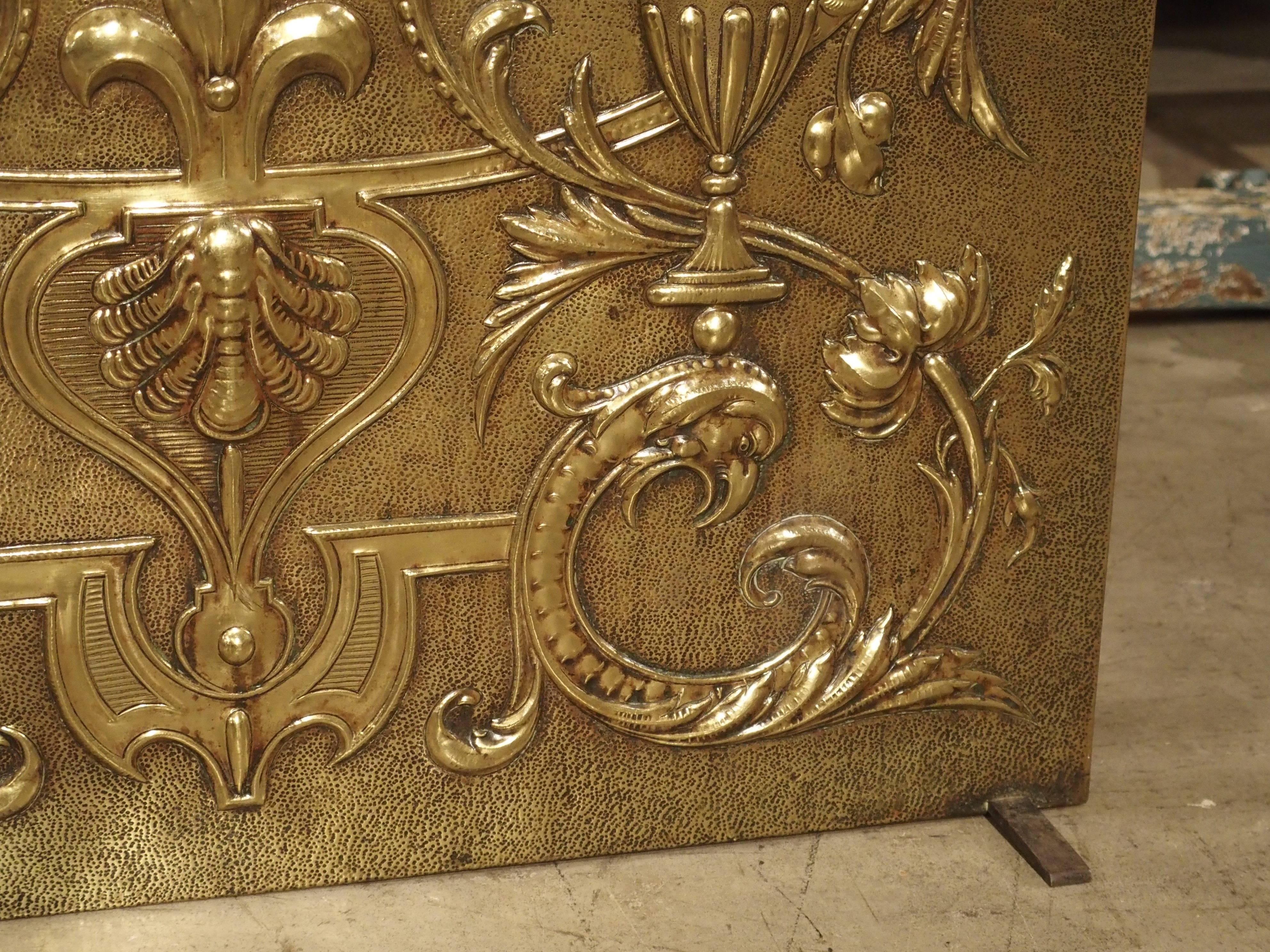 From France, this unique brass repousse fireplace screen has been exquisitely designed. Large motifs of fantastical flying animals bodies extend into the upper corners. The lower corners are half-figures of birds with leaves and flowers for their