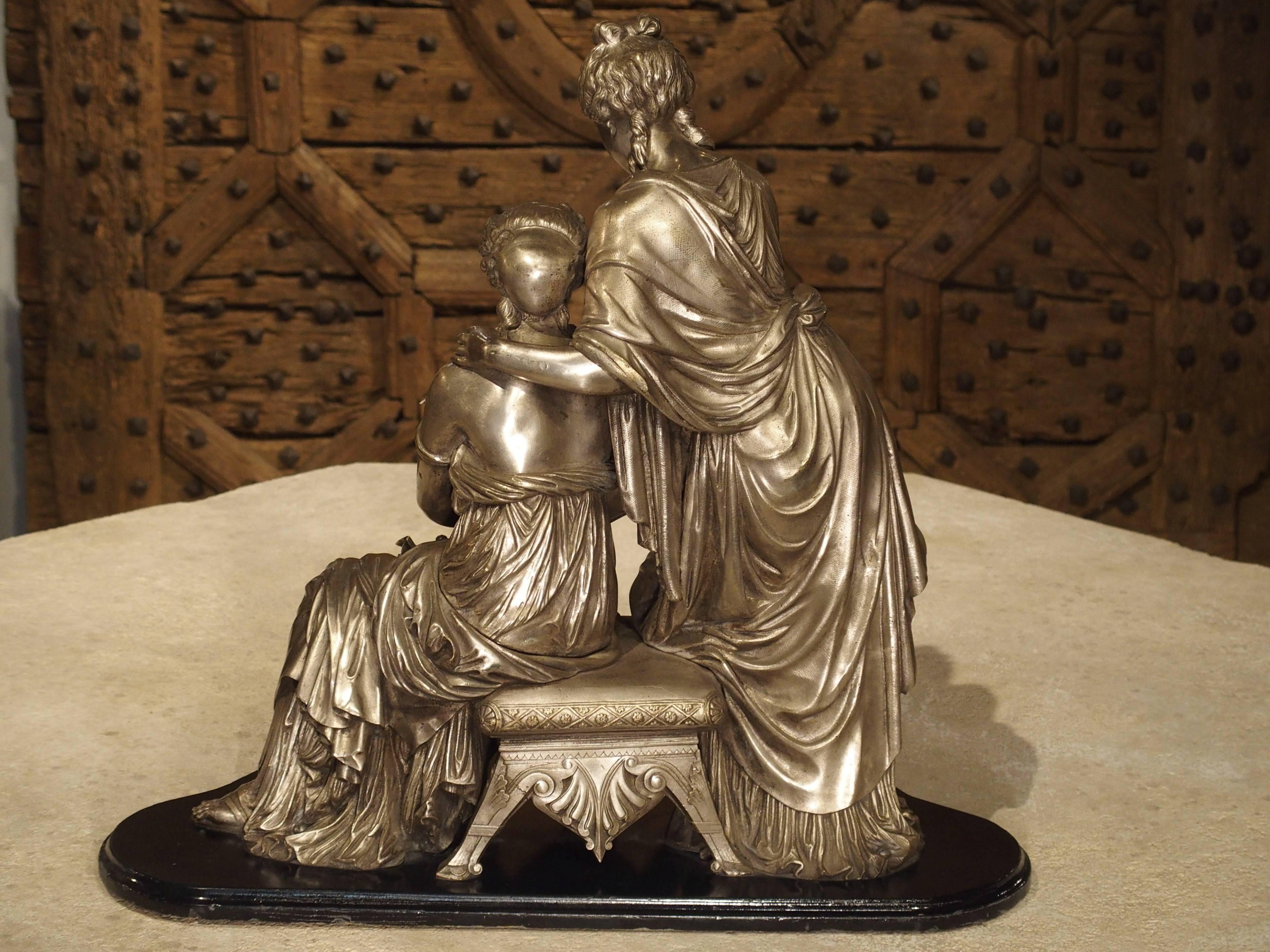 This antique French silvered bronze statuary on painted wooden base depicts two women in classical dress reading a long scroll. The woman who is seated upon a wonderfully detailed small bench, holds a writing instrument. The other woman is to her