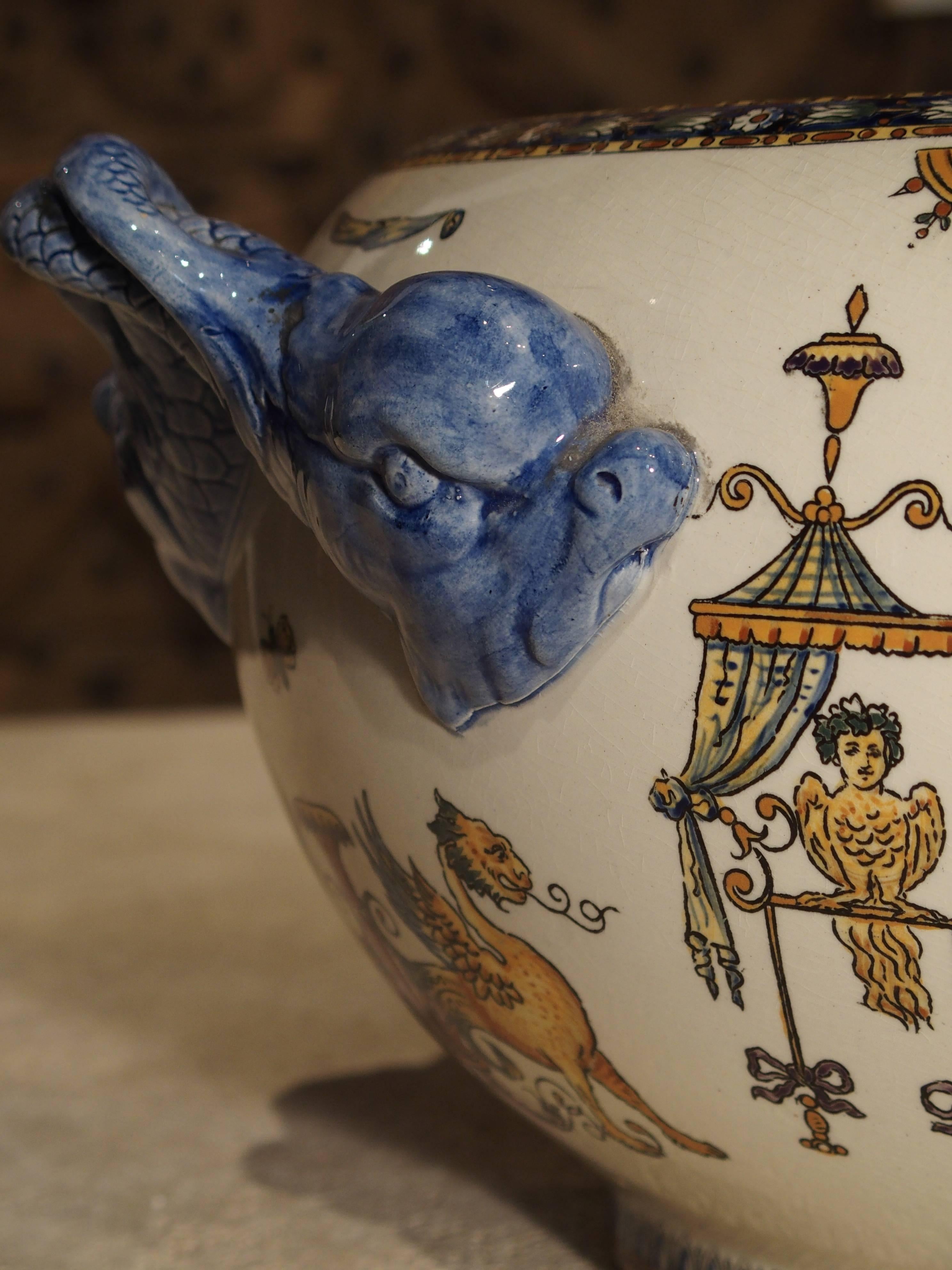 This beautiful antique French cachepot has wonderful blue dolphins for handles on either side. The white ground color is highlighted with mythological scenes. Hand-painted in golds, blues, oranges, reds, yellows and more. There is a hand-painted