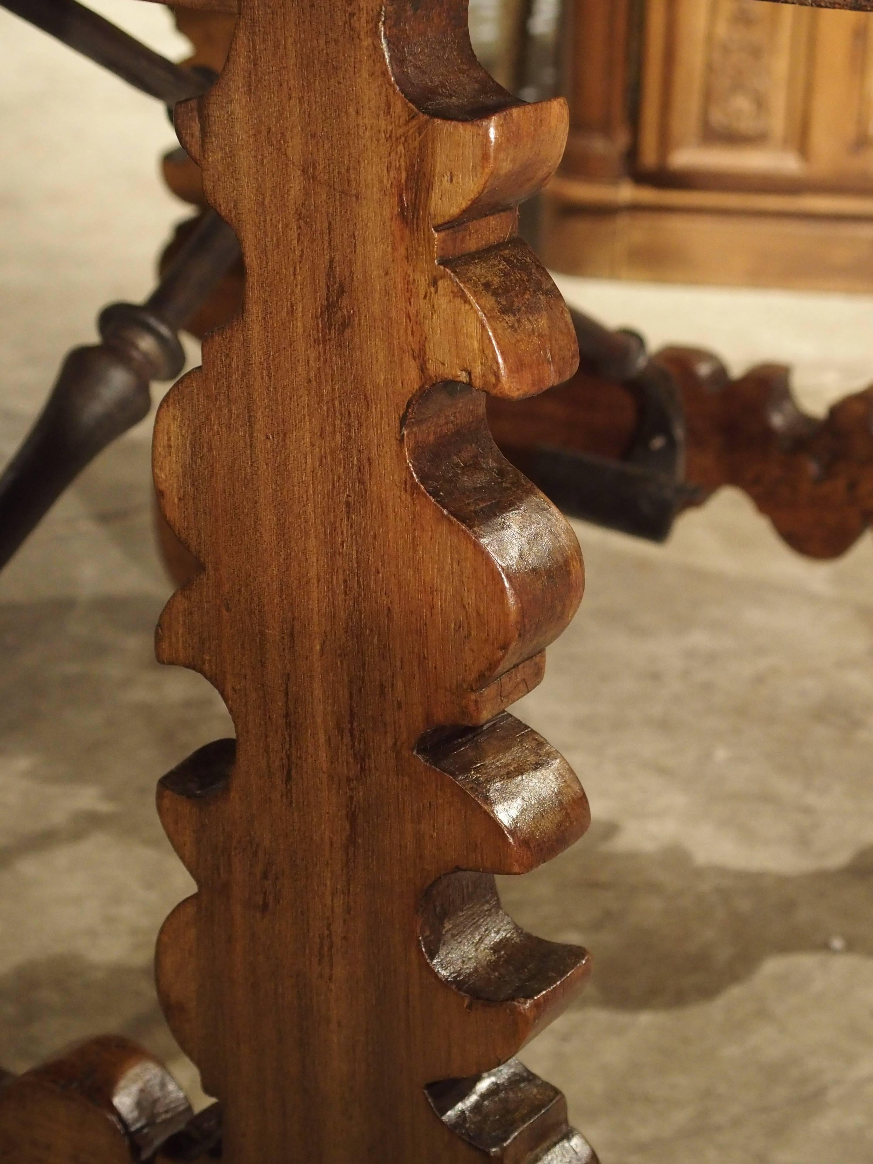 This small, hand-carved table with crossed iron stretchers is from Northern Spain and made from walnut wood. Its size is perfect for so many smaller areas of the home. It has carved ornamentation on the front drawer and the outside of the turned
