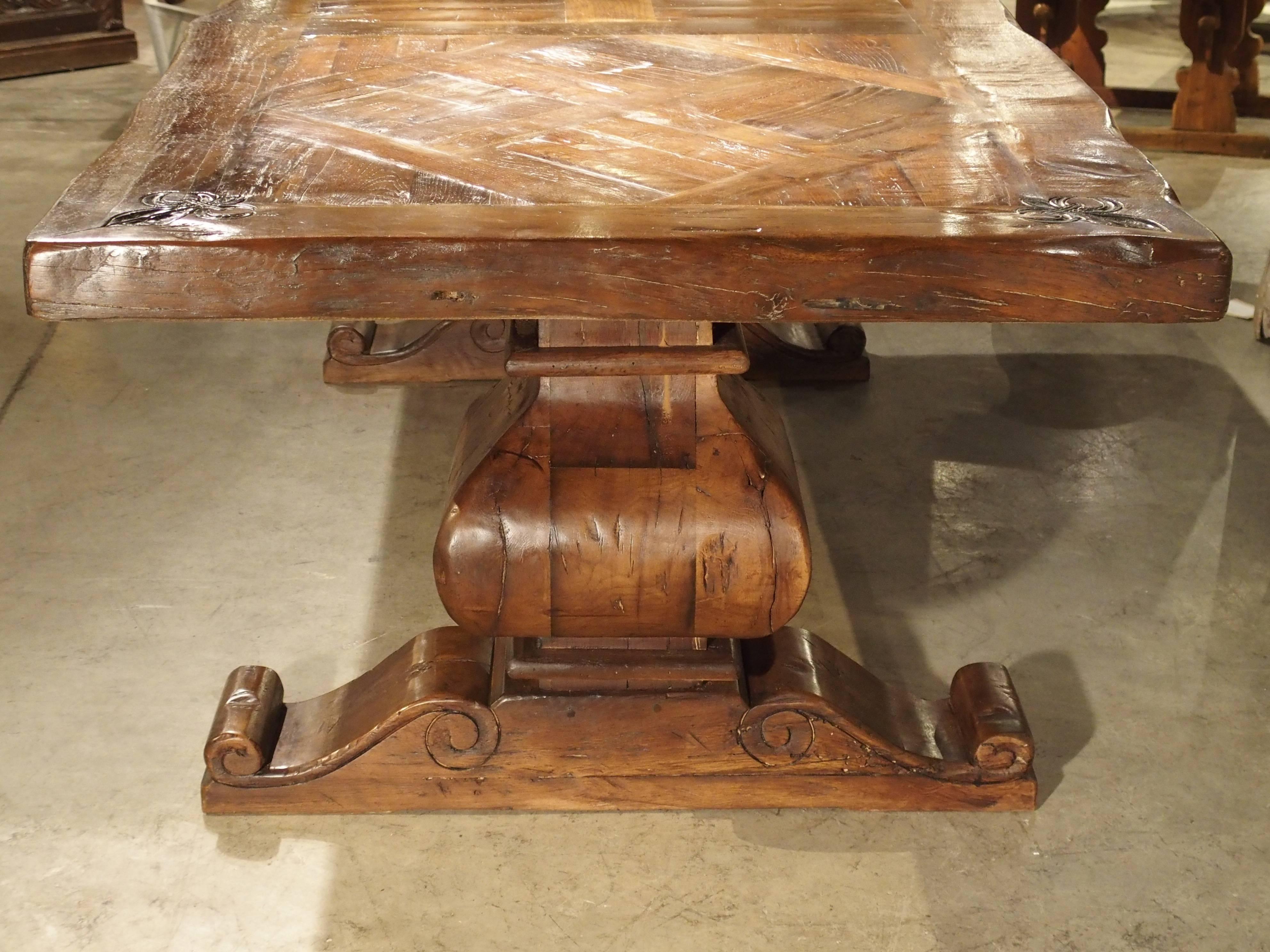 This magnificent dining room table was made in France, using oak. The top is made of two large parquet sections, separated by straight beam sections. A thick border of uneven boards encompasses the entire tabletop. At each corner of the border are