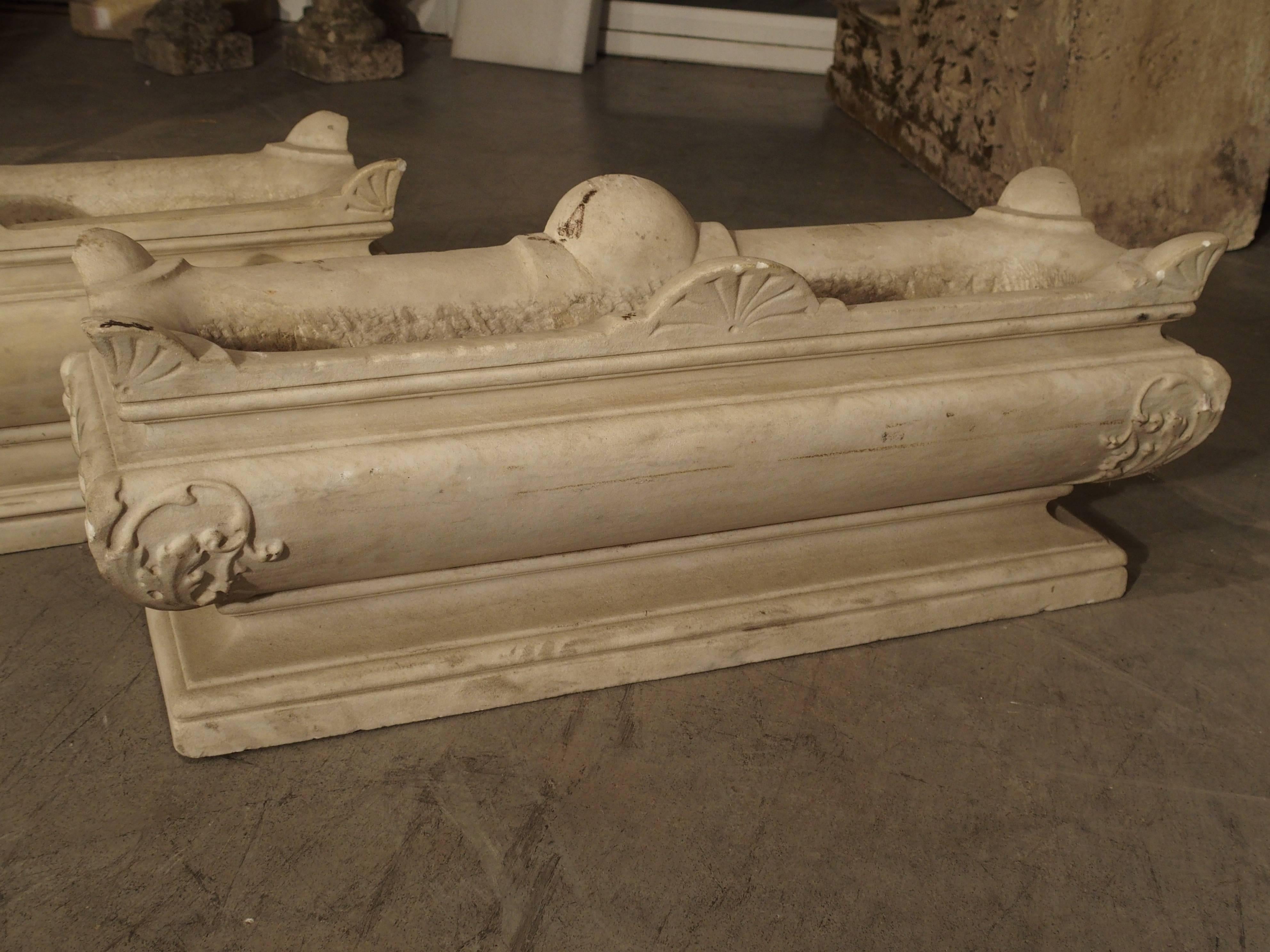 This wonderful pair of rectangular, cream colored, marble jardinières from Italy has ornamentation of stylized shells on the top rims and delicate scrolling leaves at the corners of the bodies. All of this rests upon a rectangular base. They have