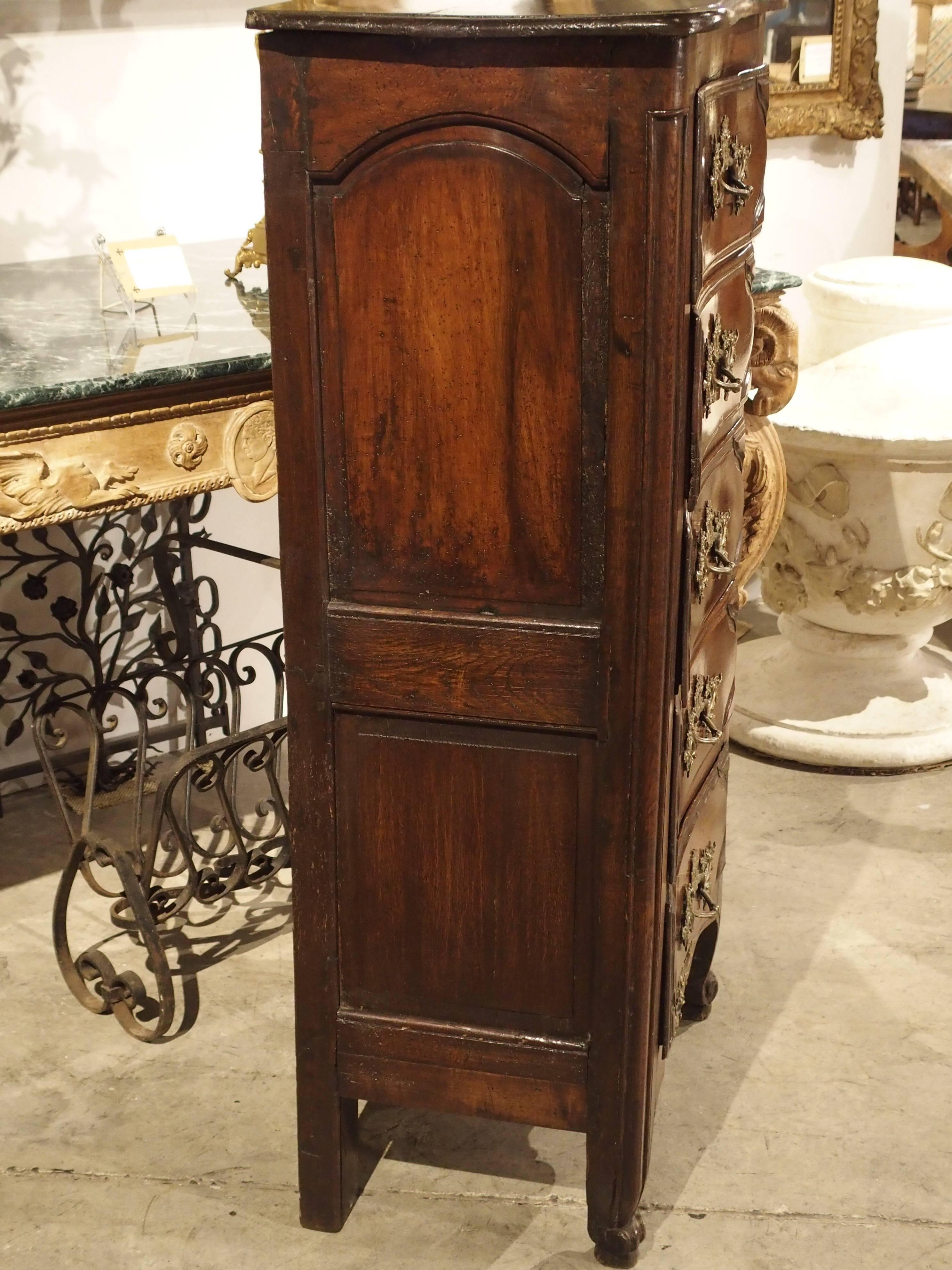 This 18th Century, five drawer commode or chiffonier from France has been made from French walnut and oak.  The top is gently shaped inward at the center front as are all of the drawers. The five drawers have been adorned with bronze Louis XV style