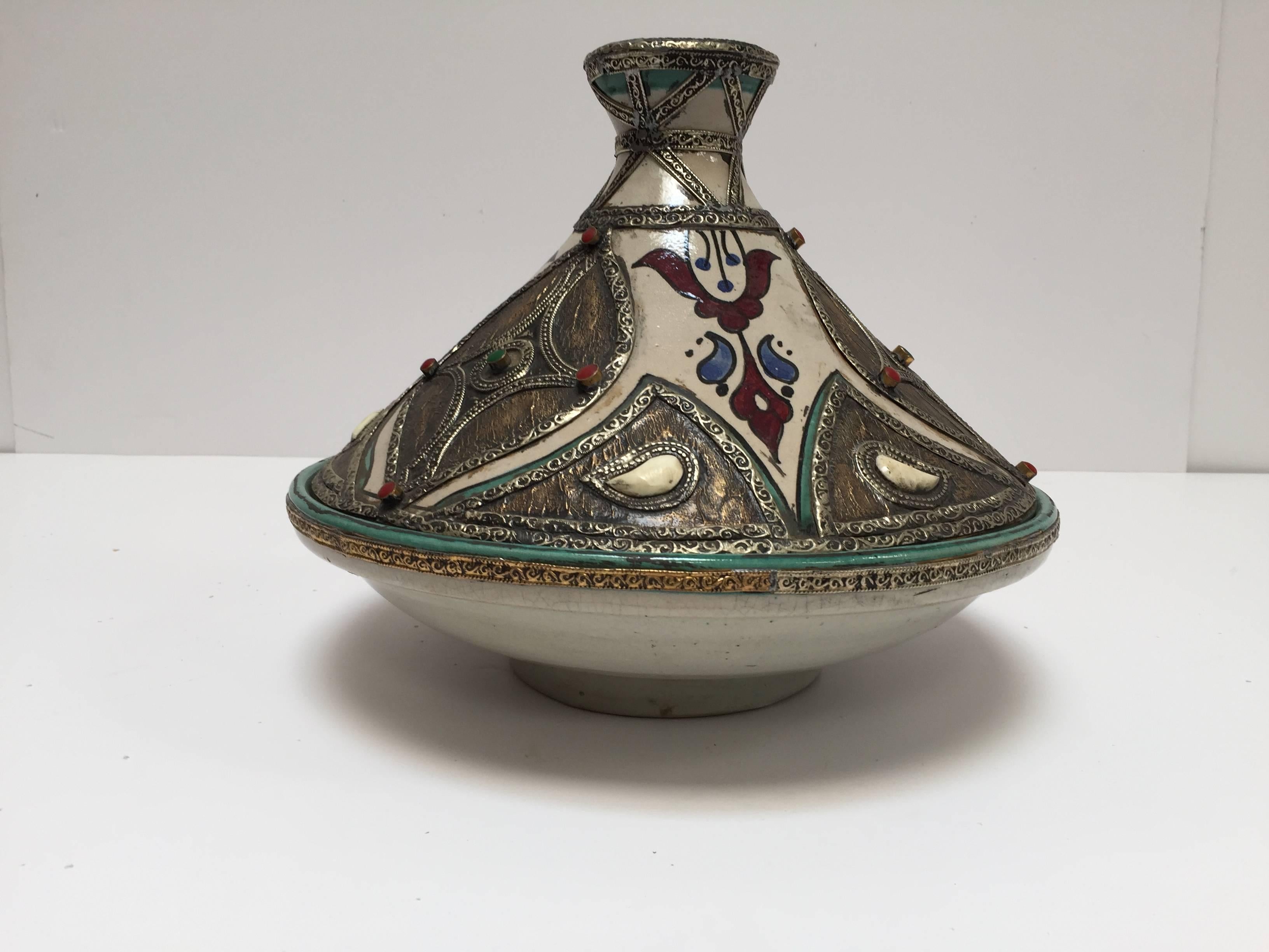 Moroccan ceramic decorative tajine polychrome with leather, stones and metal overlay with conical overlay lid.
The bottom is a circular bowl and the top of the tagine is distinctively shaped into a cone.
Handcrafted and hand-painted with Moorish