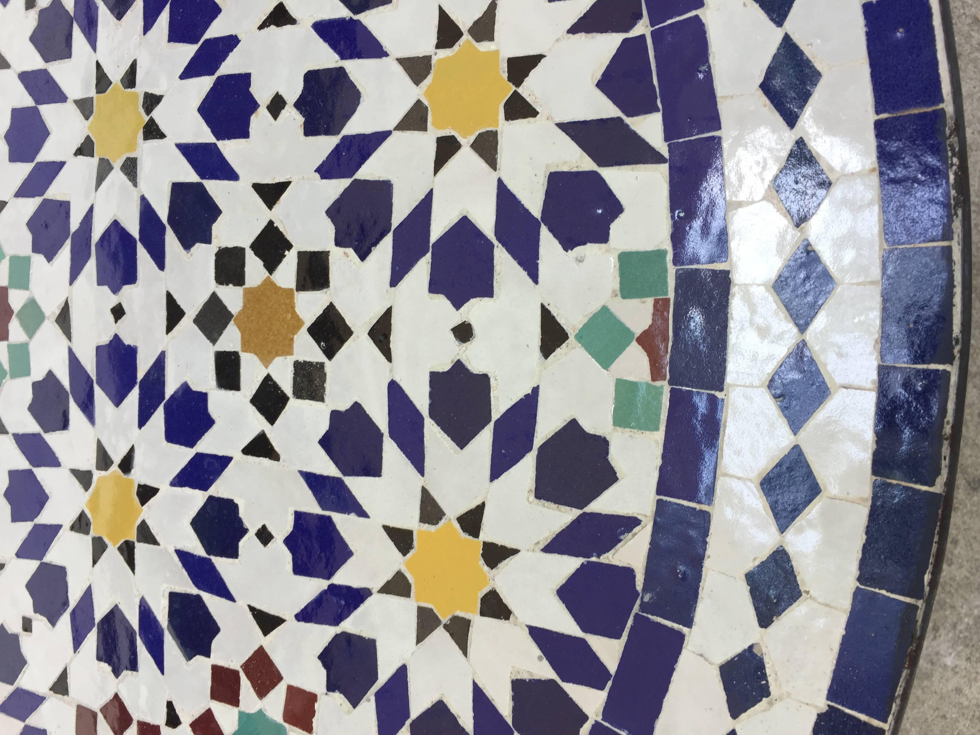 Superbe table en mosaïque marocaine, délicatement fabriquée à la main à Fès avec des motifs géométriques islamiques mauresques traditionnels dans des couleurs blanches, jaunes, bleues, rouges et vertes.
La table à carreaux repose sur une base en fer