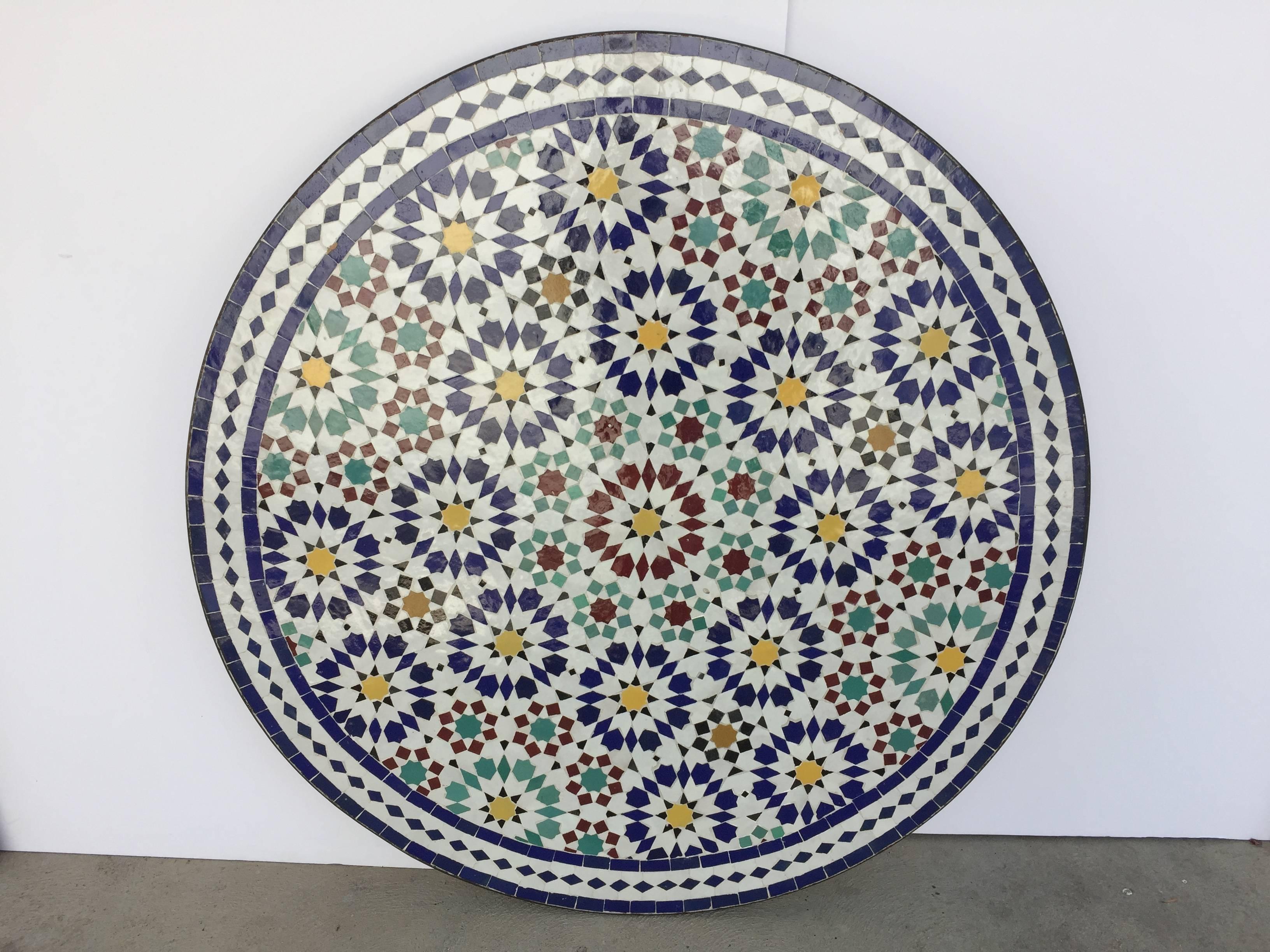 Great Moroccan mosaic round tile coffee table, delicately handcrafted in Fez with traditional Islamic Moorish geometric design in white, yellow, blue, red, green colors.
The zellige tile table sits on an iron hand-forged base in black color.
Great