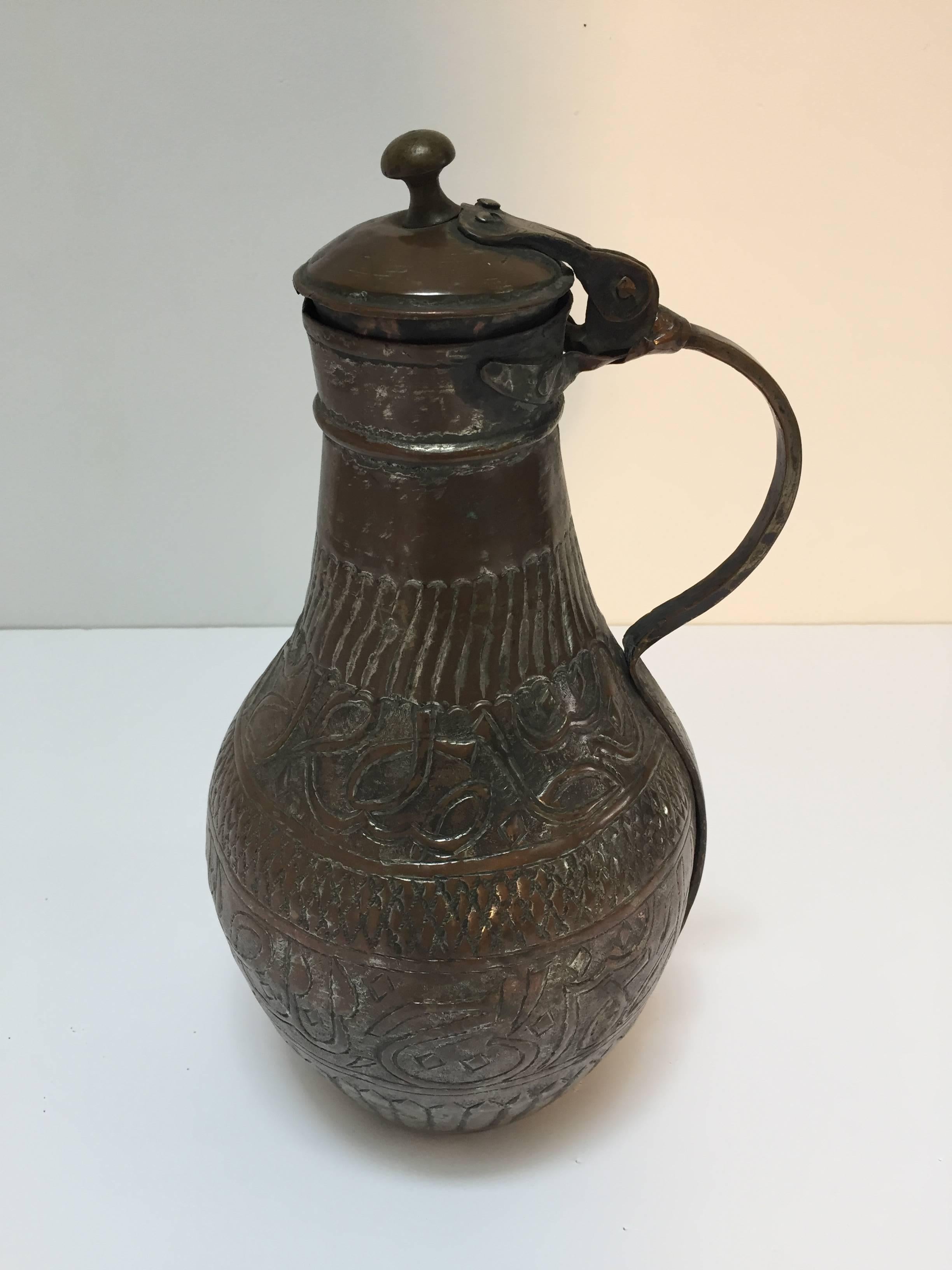 19th century Middle Eastern Arabian tinned copper ewer with lid.
Hand-hammered and chased copper with geometric design and Arabic calligraphy writing riveted finish on handle and lid.
Middle Eastern copper Moorish style ewer probably from