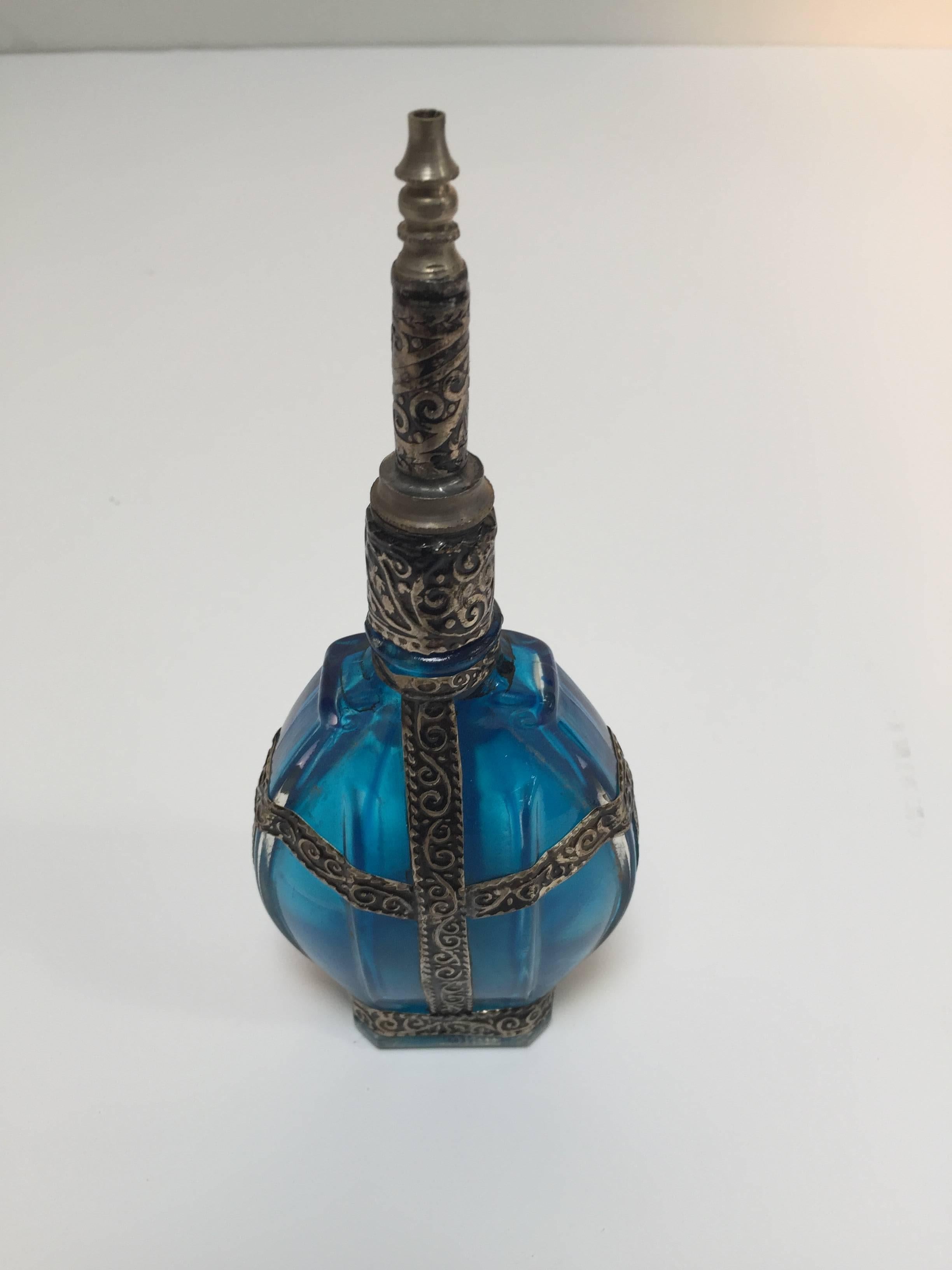 Handcrafted Ottoman style rose water sprinkler with raised embossed metal over blue glass.
The pressed glass bottle in Art Deco, Art Nouveau style is oval shape with curved sides and hand decorated with embossed metal silvered overlay. 
It has a