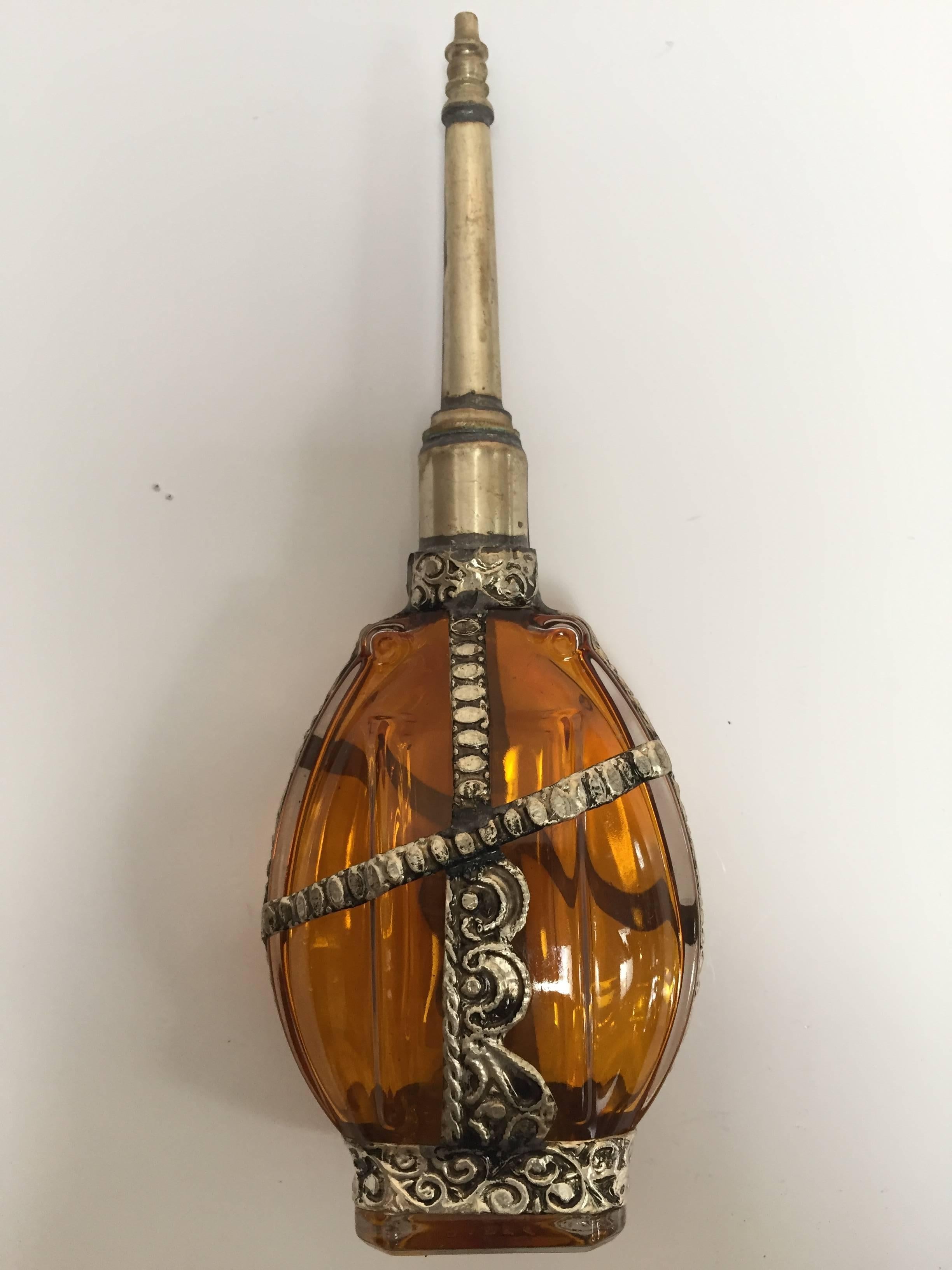 Handcrafted Moroccan Moorish glass perfume bottle or rose water sprinkler with raised embossed silvered metal floral design over amber glass.
The pressed glass bottle in Art Deco, Art Nouveau style is oval shape with curved sides and hand decorated