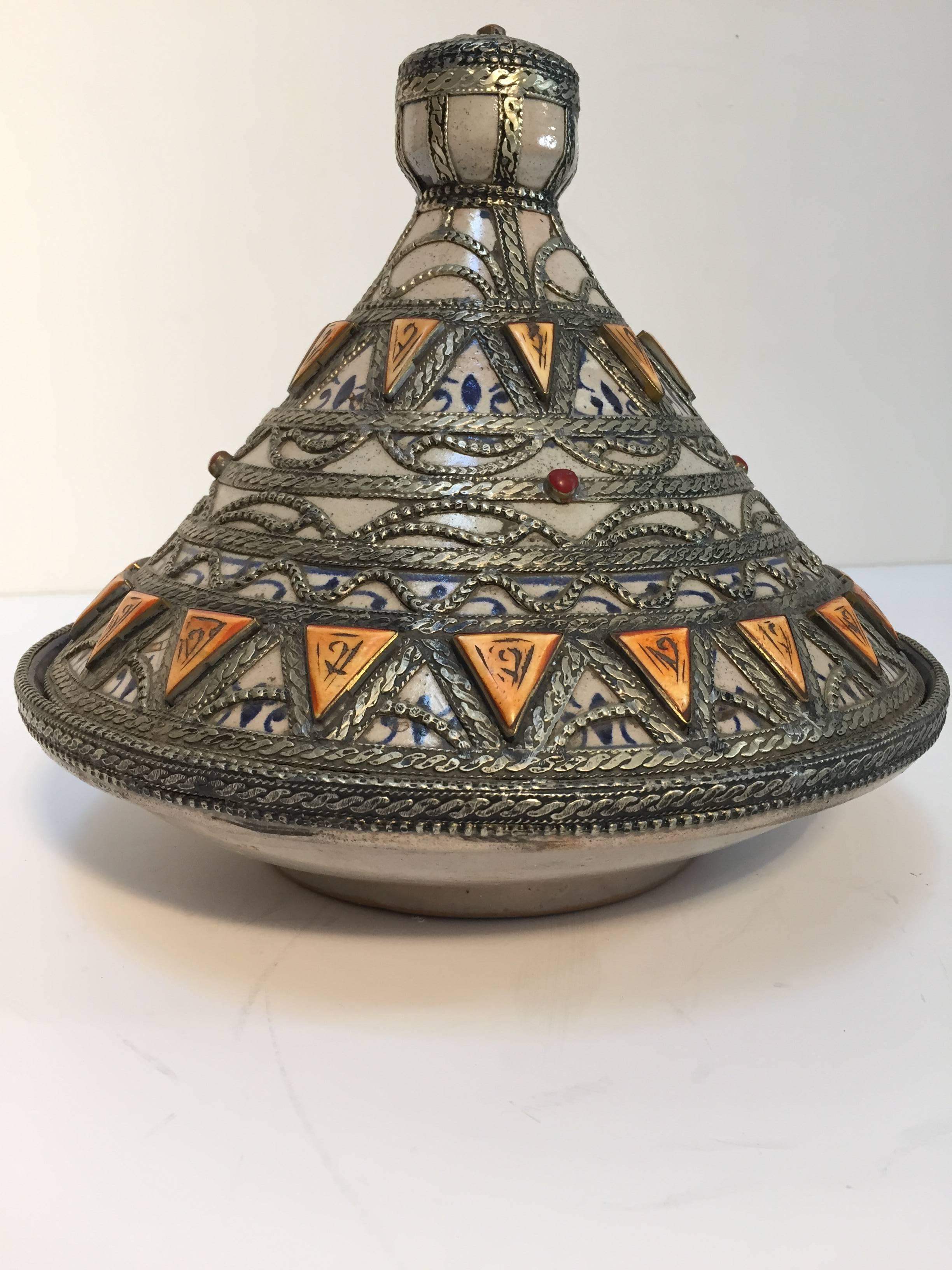 Moroccan ceramic decorative tajine polychrome with leather, stones and metal overlay with conical lid.
The bottom is a circular ceramic bowl hand painted in blue and white Moorish designs and the top of the tagine is distinctively shaped into a cone