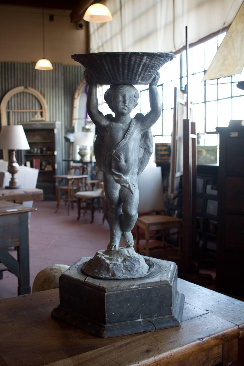 Antique English lead putto holding a bowl above his head, standing on Victorian wooden plinth. Plinth not original to putto.