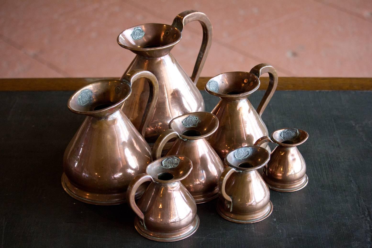 Set of seven antique graduated copper jugs from 1/8th of a gill to 1 quart. These jugs were used to measure ales, ciders and spirits in old British inns. They have a lead H R seal which was applied by Customs and Excise to ensure the inn owner was