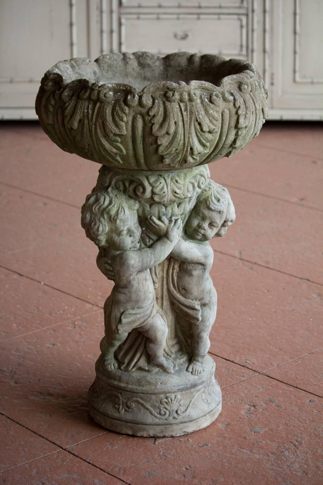 Whimsical English vintage composite stone jardinière with a trio of putti holding up a bowl draped in acanthus leaves. Wonderful patina.