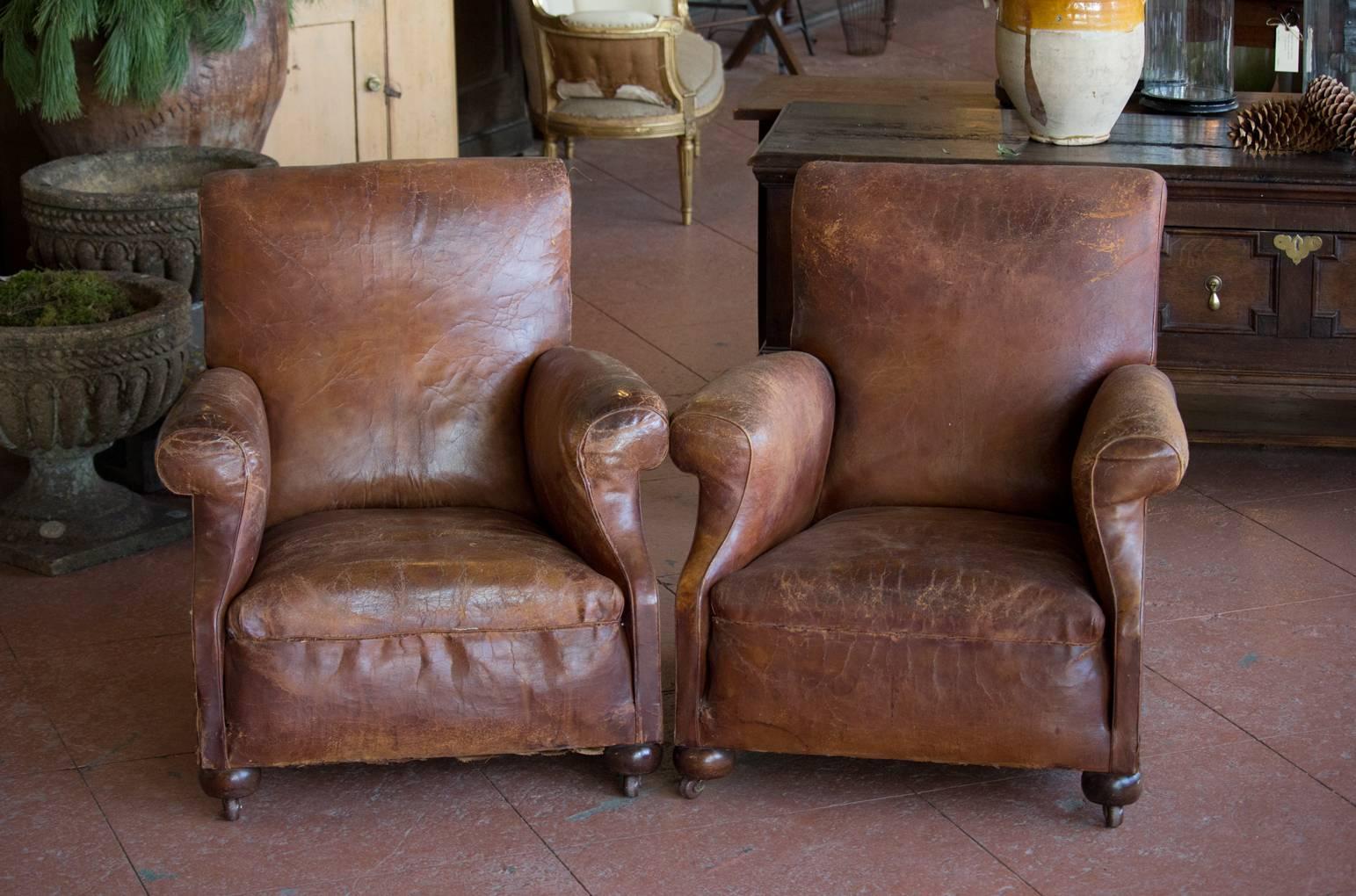 Pair of substantial English vintage leather club chairs with slight roll arm and back design. Each chair sits on front bun feet with four original casters. Just enough scruffiness to be totally chic and charming!