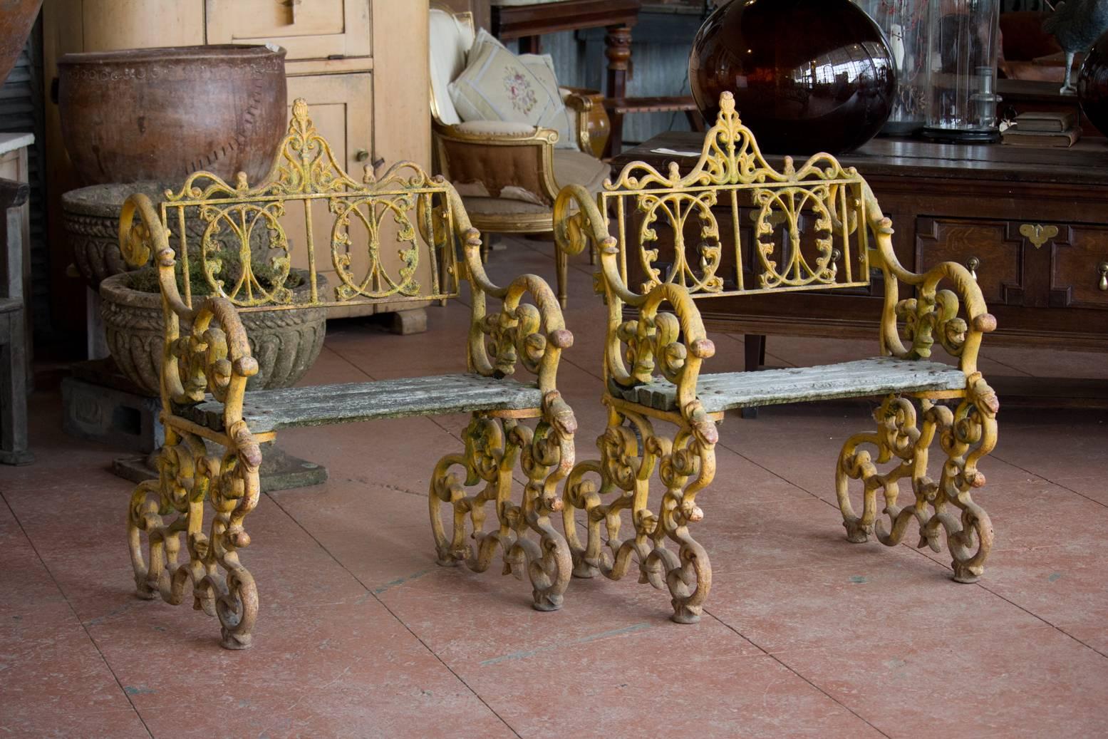 Pair of highly decorative vintage cast iron British pier benches with original mustard paint.