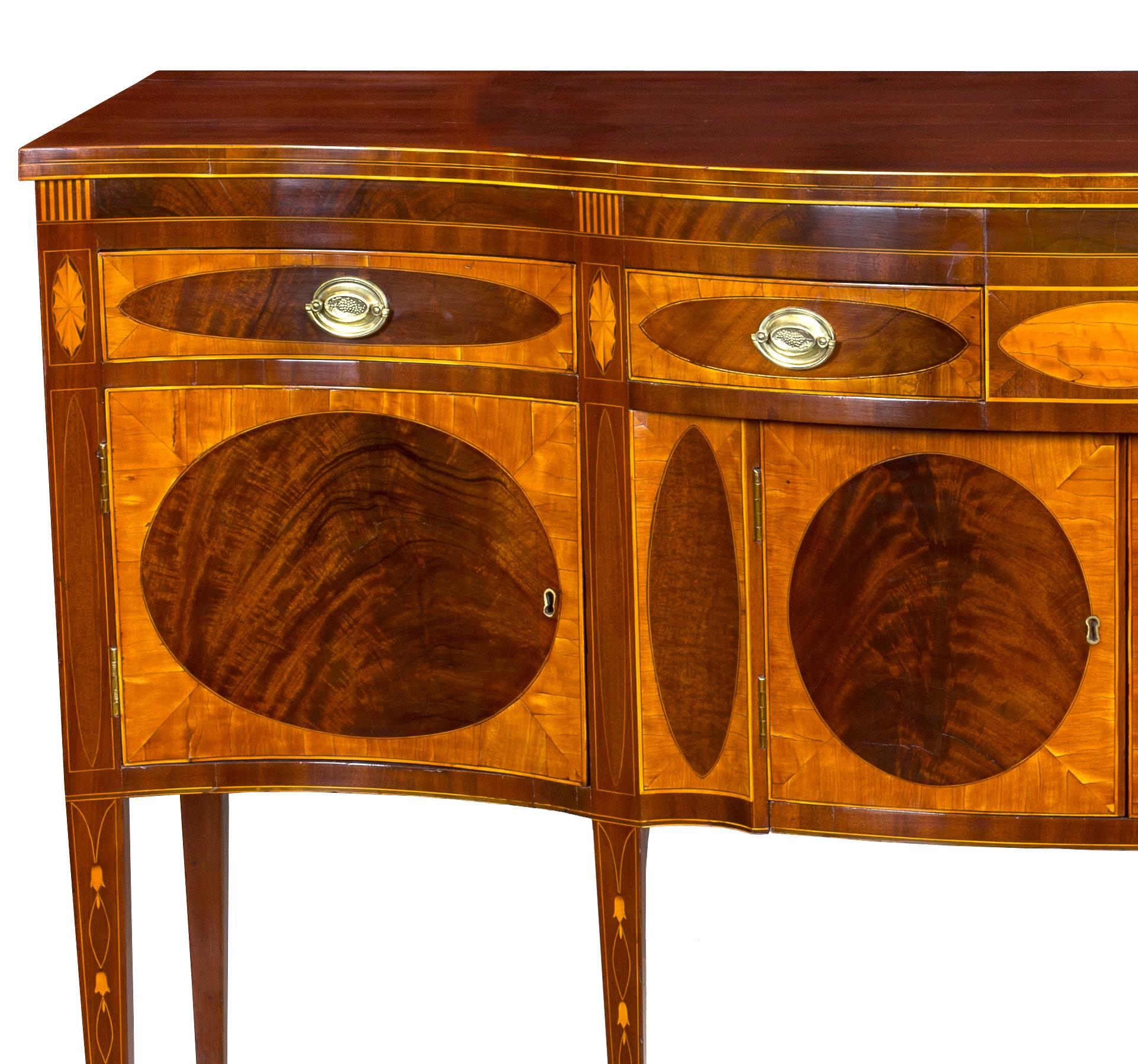 This is one of the finest sideboards in our collection and is composed of brilliant rarely found satinwood and profusely inlaid with bellflowers, patera and line inlay. It is of serpentine form, which is the most desirable form that these sideboards