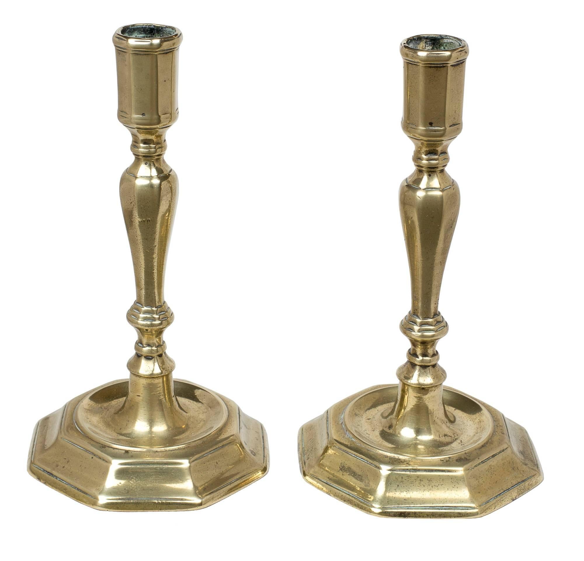 These candlesticks have a molded octagonal base with knapped baluster standard and paneled or cylindrical nozzle.

A related candlestick of similar design and origin is illustrated in The Brass Book, by Peter, Nancy, and Herbert Schiffer (see scan