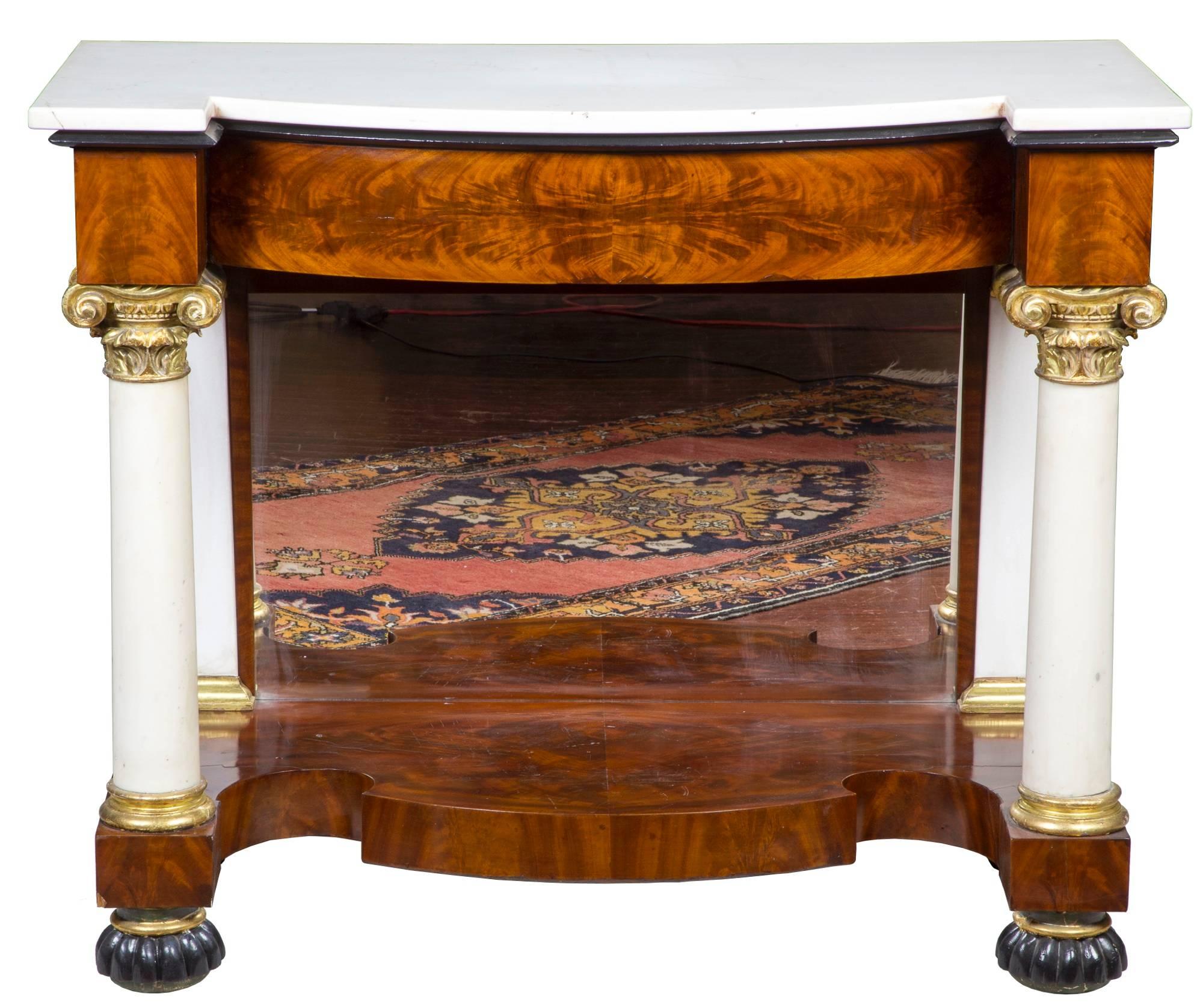 These pier tables are composed of vibrantly figured mahogany with marble columns which are held in place by strongly carved capitals. The capitals are gilt, as are other elements on these tables. These pier tables also have marble pilasters in the