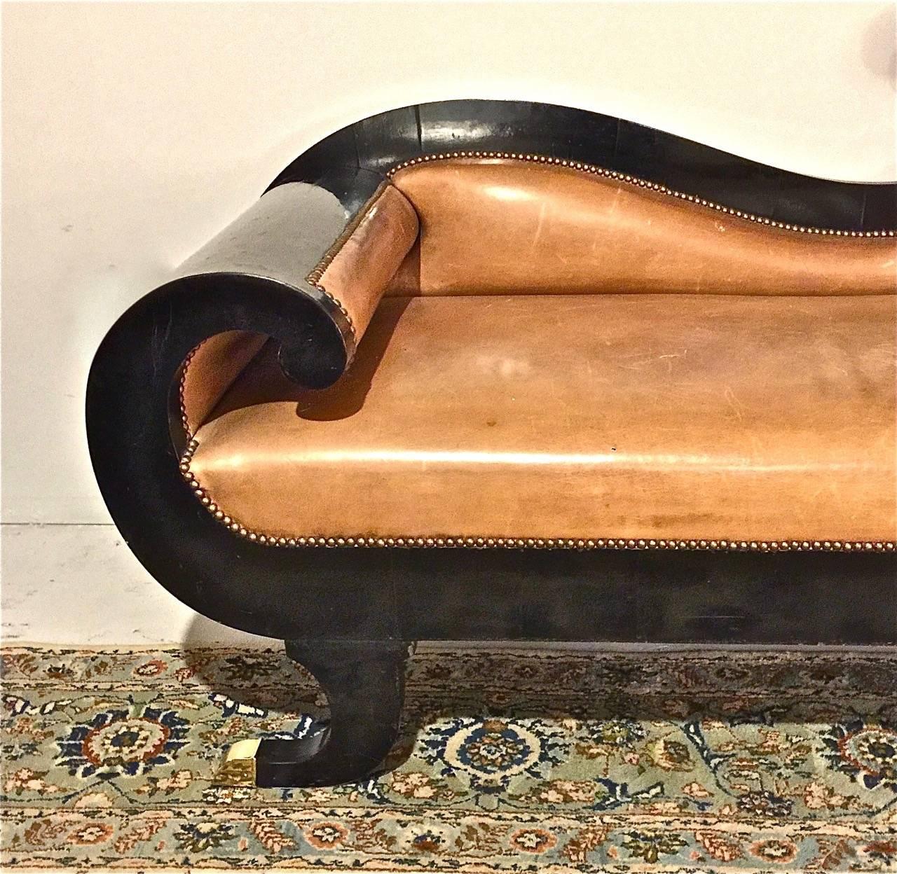 Stunning period English late Regency, circa1830-1840 recamier or sofa. I believe that the recamier retains its original black lacquer finish which has been recently polished; it is upholstered in a light caramel-toned leather which has acquired just