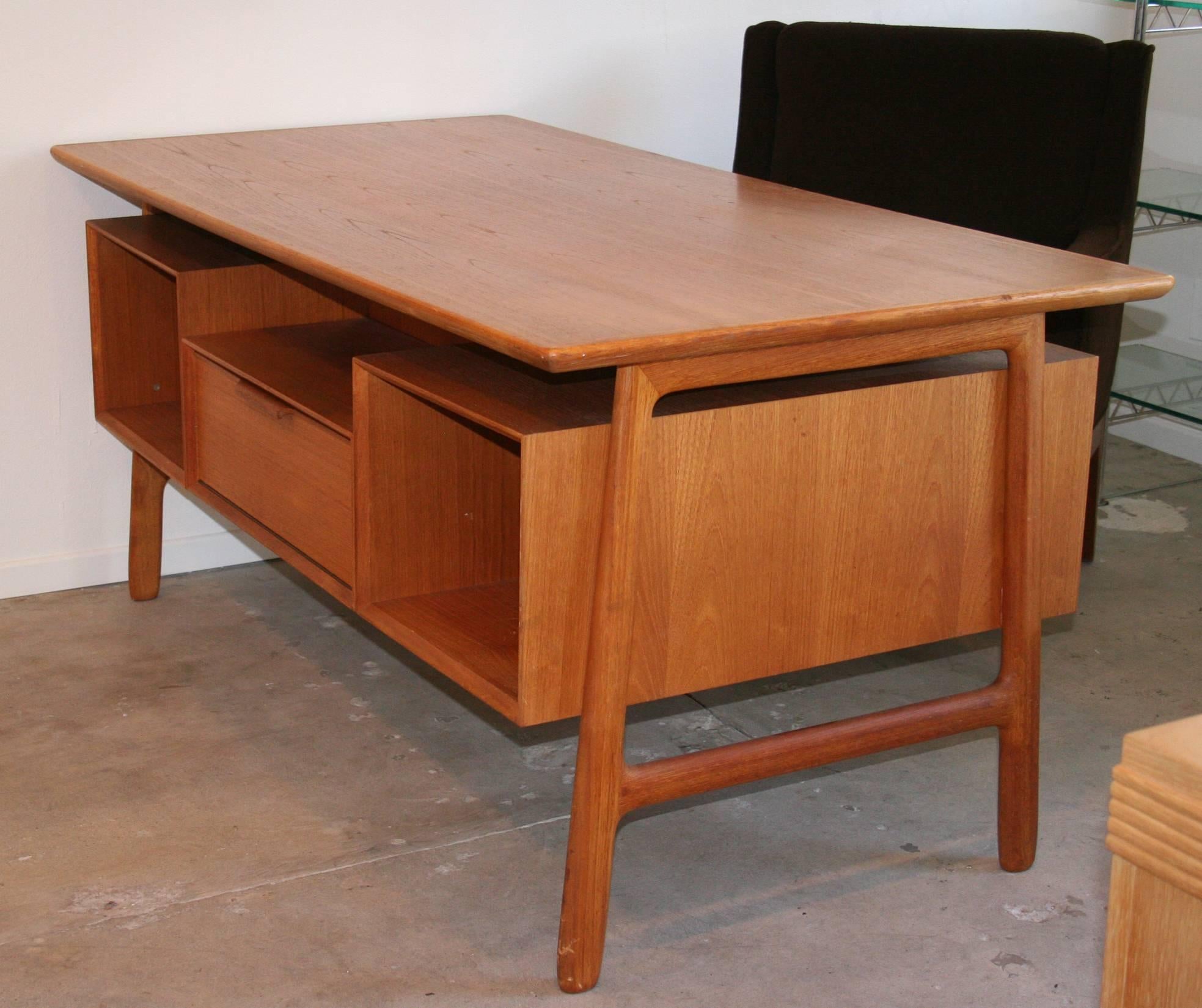 A Danish double pedestal desk in teak with floating top by Omann Jun Møbelfabrik. On desk side, three drawers in one bank and a file drawer in the other. On the opposite side, book cubbies flank a central drop front cabinet.