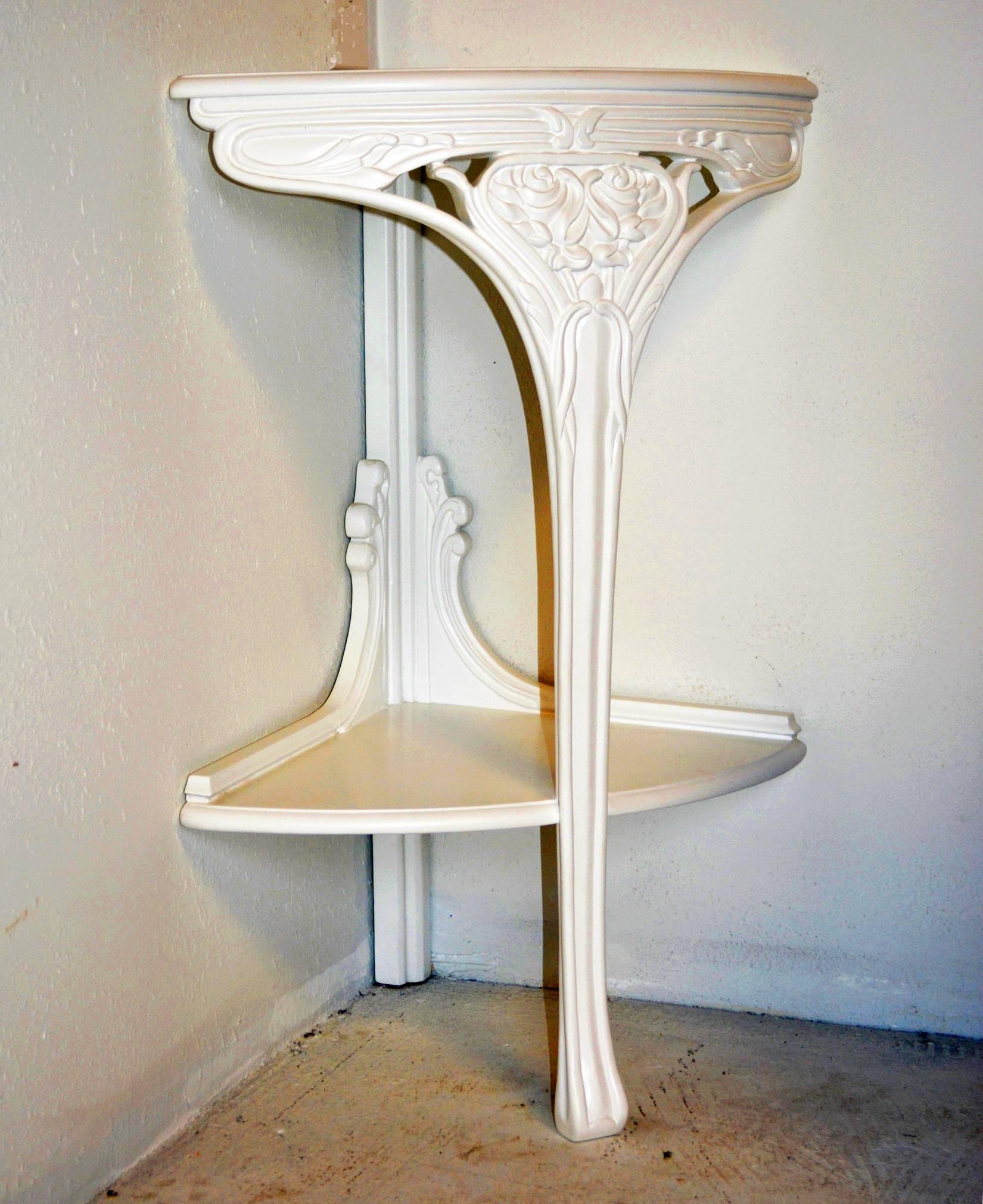 A chic pair of Art Nouveau carved encoignure (corner tables) lacquered ivory. Central splayed foot leg, supporting a lower shelf, rises to a carved apron.