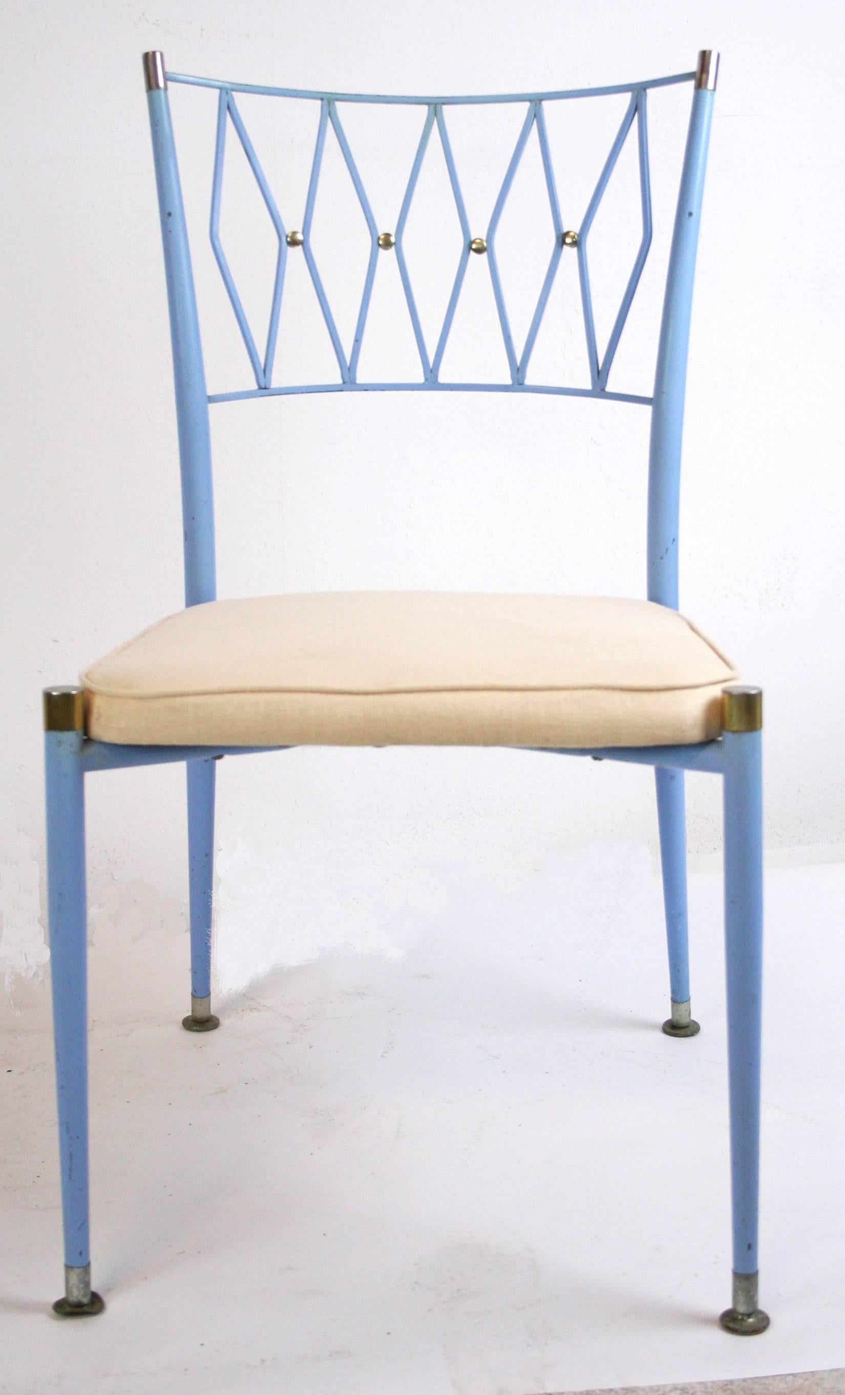 A chic set of four dining chairs in painted metal with brass accents in the style of Colette Gueden or Maison Jansen. Original French blue paint and upholstered seats. Elegant stylized lattice back splat with brass "buttons" and chrome