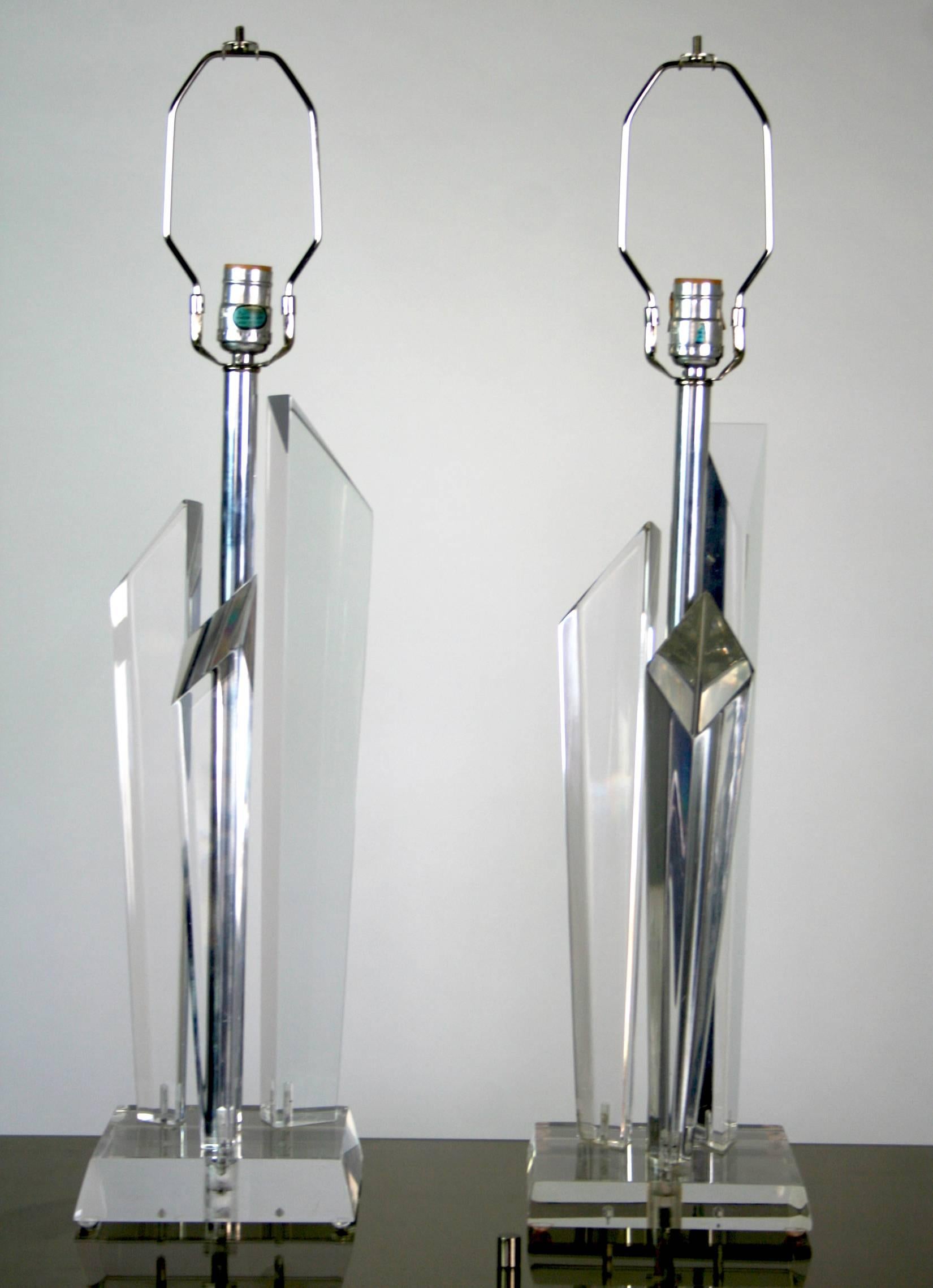 A pair of Lucite lamps each with three Lucite tapered prisms with angled tops on a Lucite base. The assemblage reflects and refracts light. Central chrome rod supports a socket and harp.