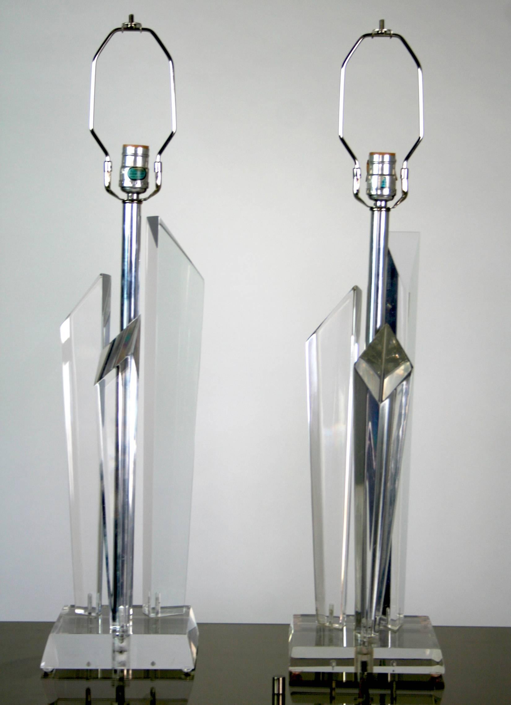 Paire de lampes en Lucite comprenant chacune trois prismes effilés en Lucite avec des sommets angulaires sur une base en Lucite. L'assemblage reflète et réfracte la lumière. La tige centrale chromée supporte une douille et une harpe.
