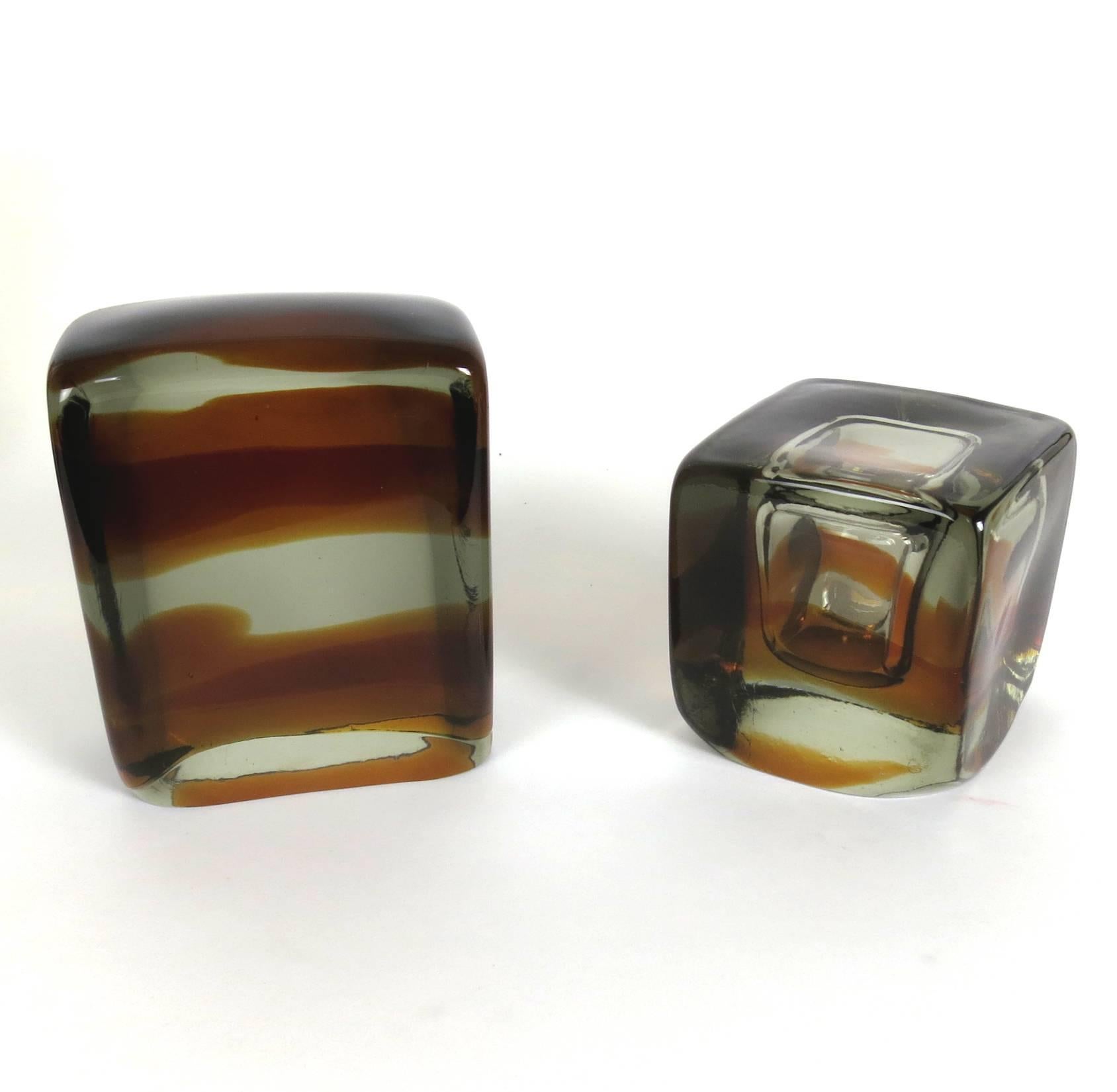 A pair of Murano glass bookends, unmarked, clear glass with amber glass. One is a cube with a bubble void, the other is a rectangular slab. Measures: 4.75" W x 4.75" D x 4.75" H; 6" W x 3" D x 7" H.