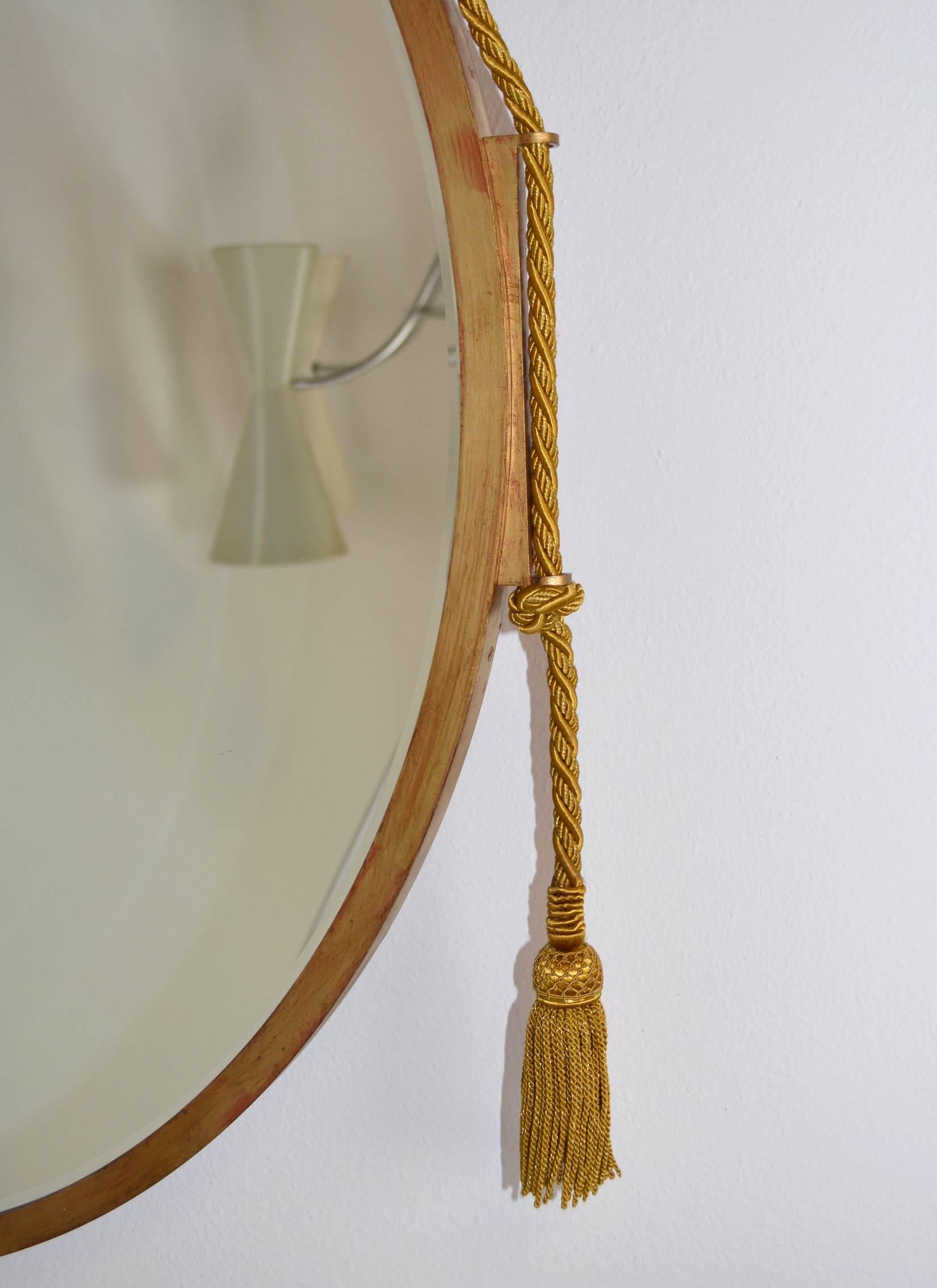 A lovely large beveled mirror with a gilt metal frame, hung on gold rope with tassel ends. In the style of Emile-Jacques Ruhlmann. Measures: 35 1/2" diameter currently hung on one rope, but can be hung from two ropes as shown in the last photo. 