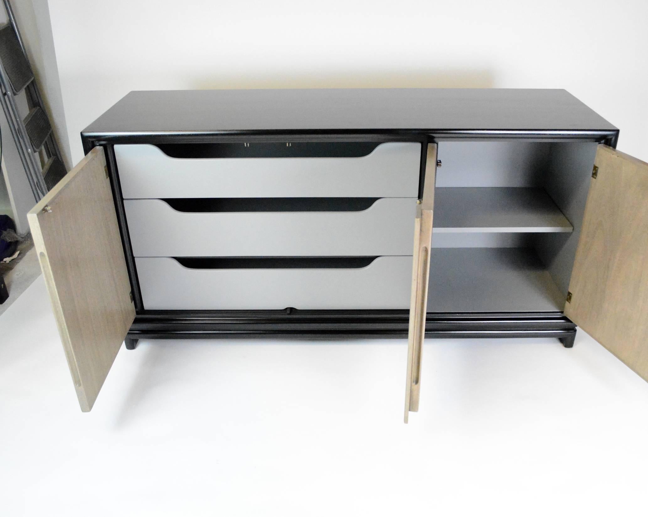 A black lacquered Mid-Century Modern three-door credenza buffet, opening to reveal drawers on left side and a shelf behind the right door. doors in a bleached grey washed mahogany veneer. Newly refinished.