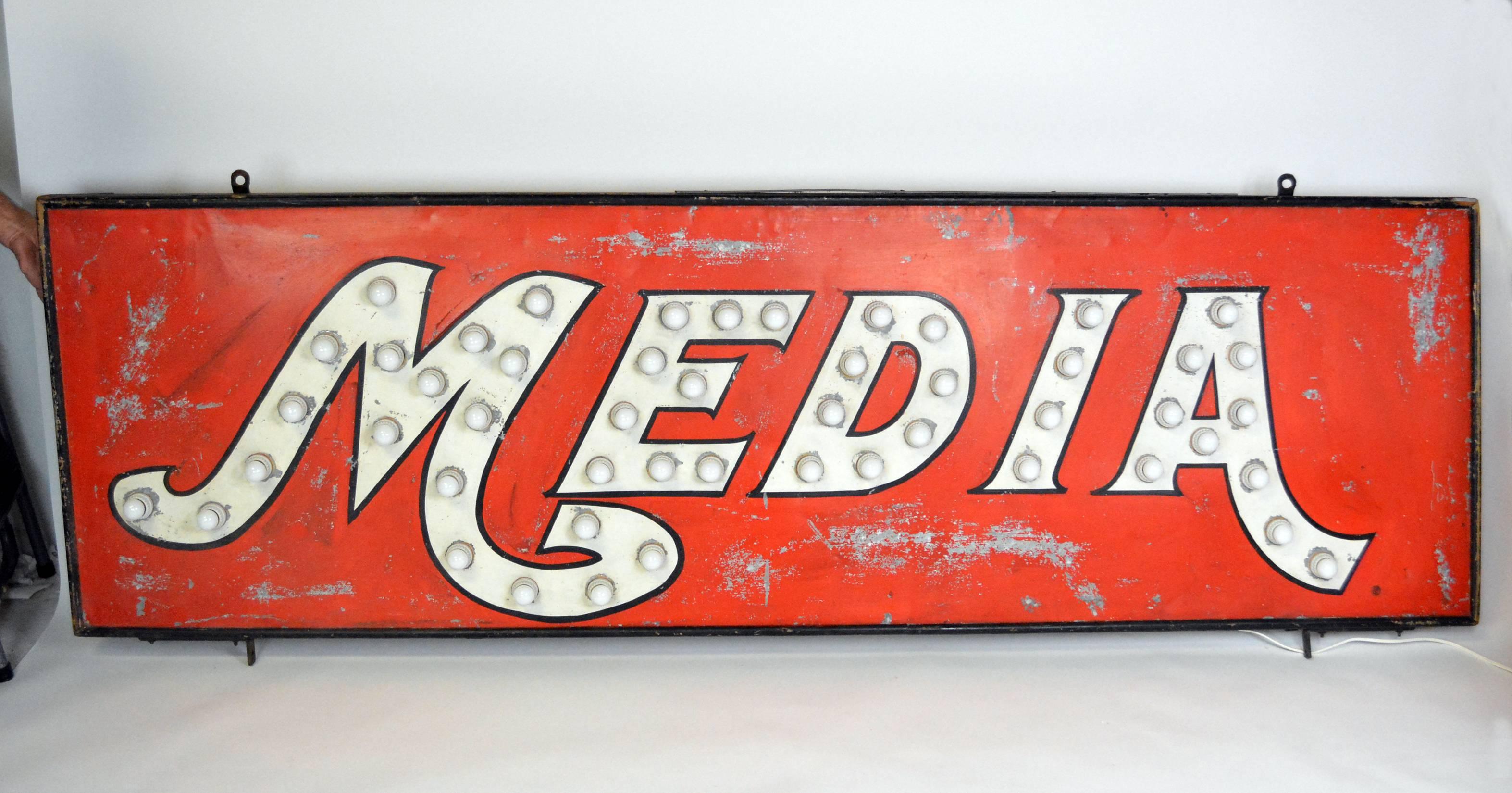 An antique folk art metal sign with a wood frame and original painted surface, a red background with 'Media' in white script outlined in black. The letters have a total of 50 wired bulb sockets. Sockets and all wiring has been replaced. Truly unique.