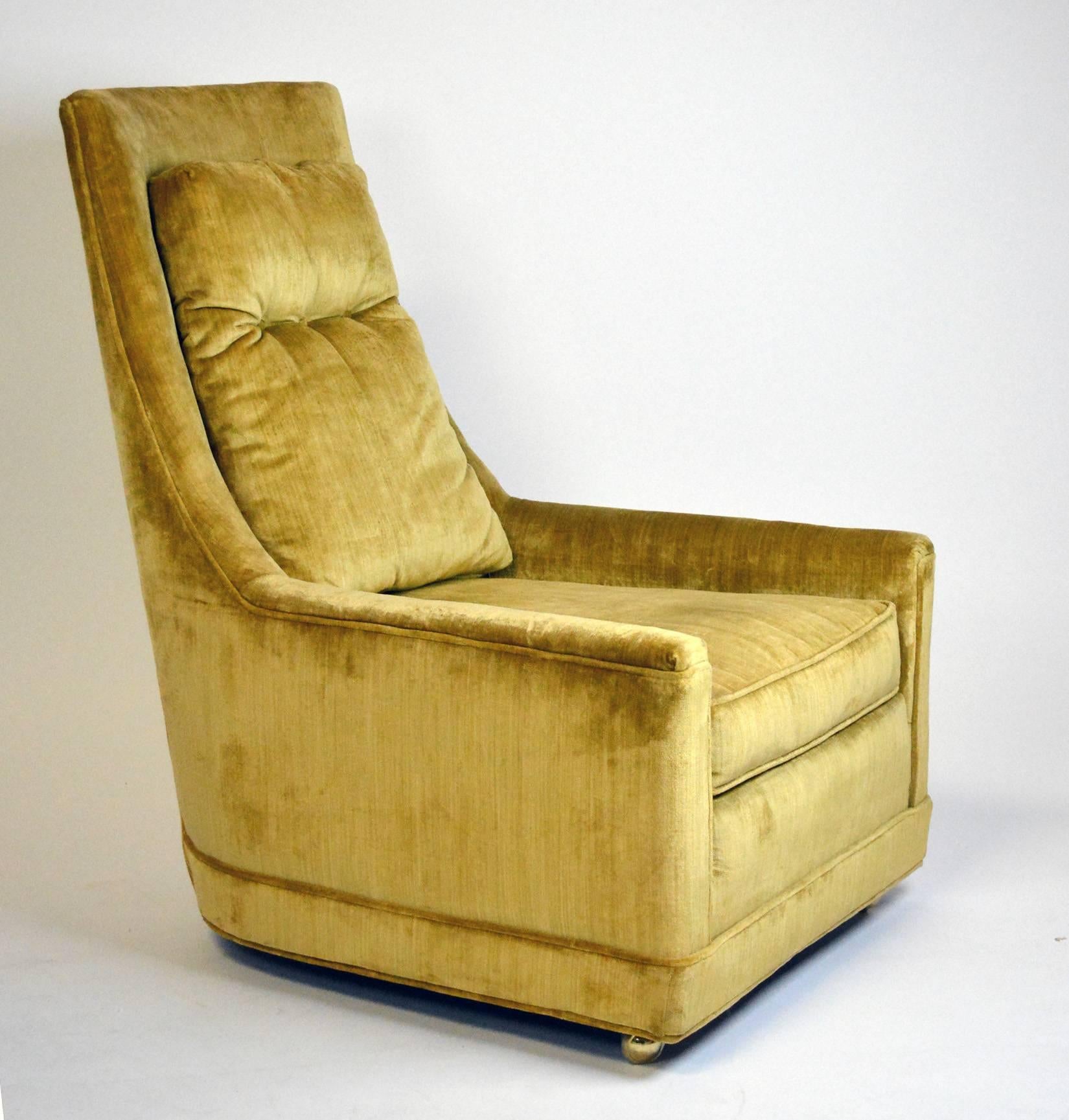 A pair of 1970s glam Hollywood Regency high back lounge chairs in original velvet upholstery. The low arm swoops up to a high back with a loose back cushion, tufted with three buttons. The chairs are on casters at the front and legs at the back.