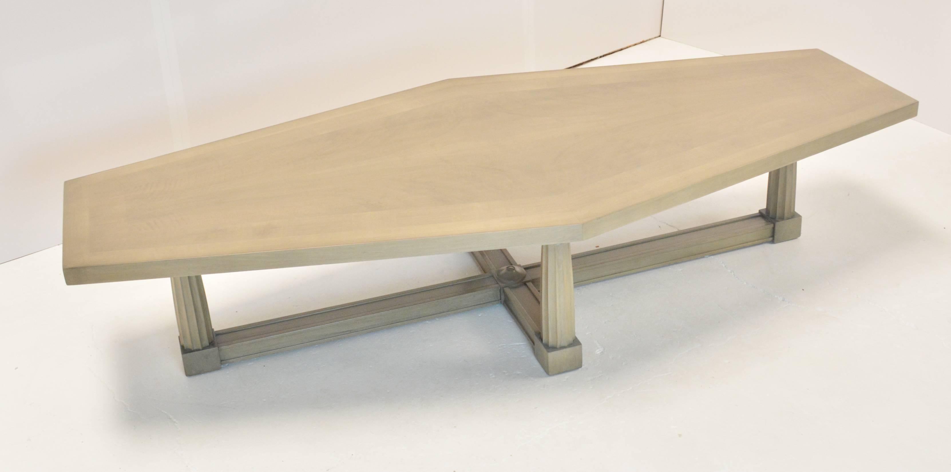 A Baker coffee table, circa 1960, with a elongated diamond like top on four Doric column legs on a cross stretcher. Top is inlaid with figured and flamed bleached mahogany, in a grey/silver finish.