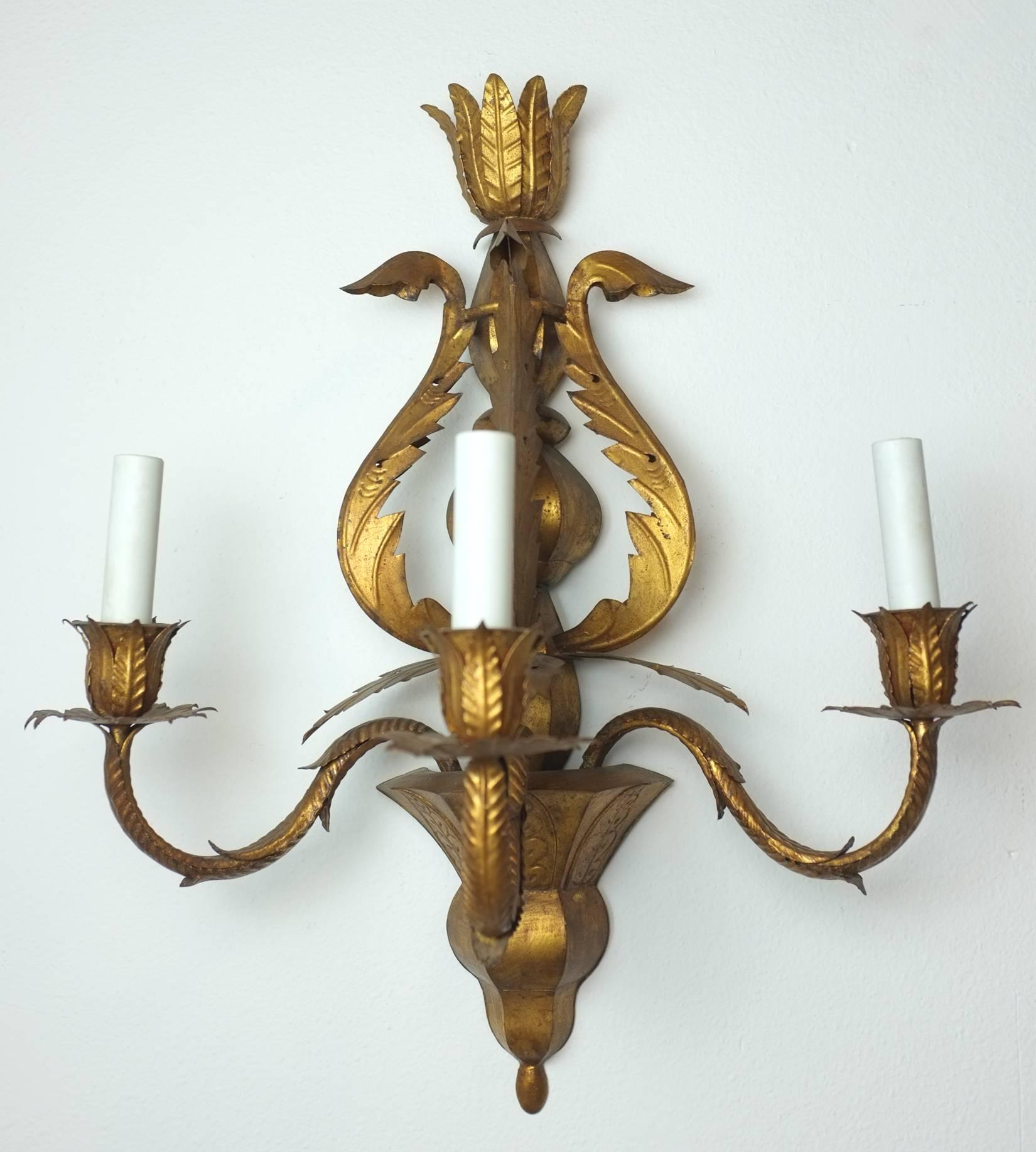 A pair of three-light gilt tole sconces, Spanish, circa 1950s or 1960s. Scrolling leaves form a central figure with three scolled arms ending in leaf bobeche and 'cups'. Rewired. Takes a max 25 watt candelabra base bulb.
  
