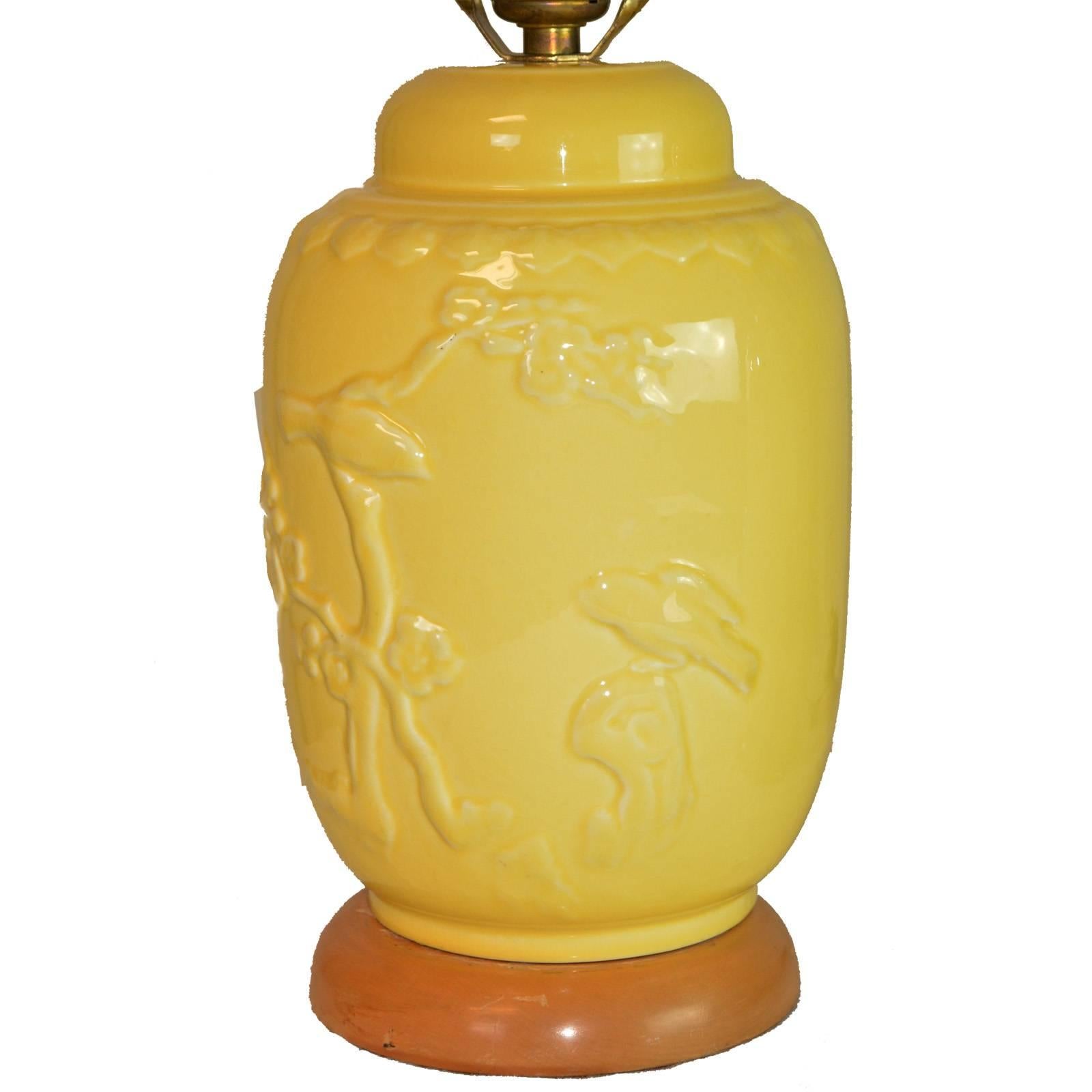 A pair of small-scale Mid-Century Modern ceramic lamps. A vibrant yellow glaze animates an Asian inspired scene of a bird on a leafy branch in raised decoration on a jar shape form, with original blond wood base and matching ceramic finial.