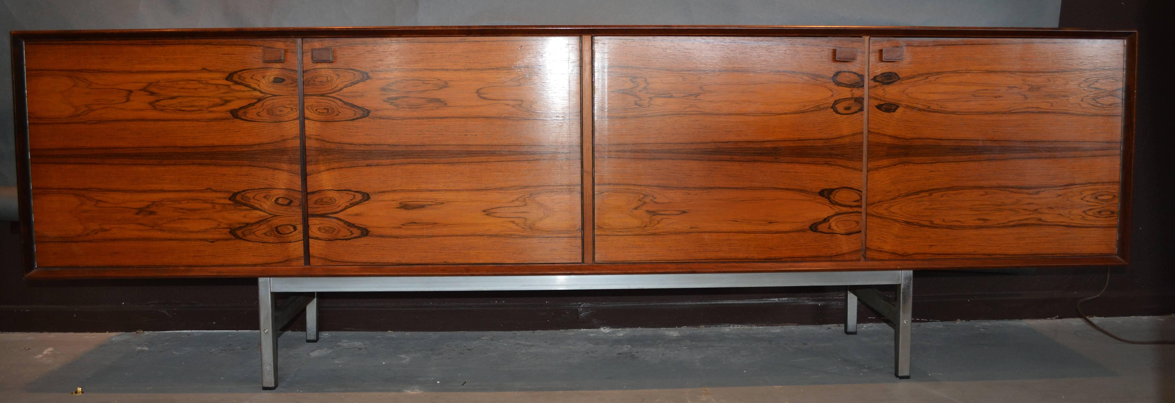 A Danish or possibly German credenza of beautifully bookmatched rosewood veneers consisting of four doors with unique wood handles. A set of drawers and shelves behind the right set of doors, and a single shelf in the left portion. The whole resting