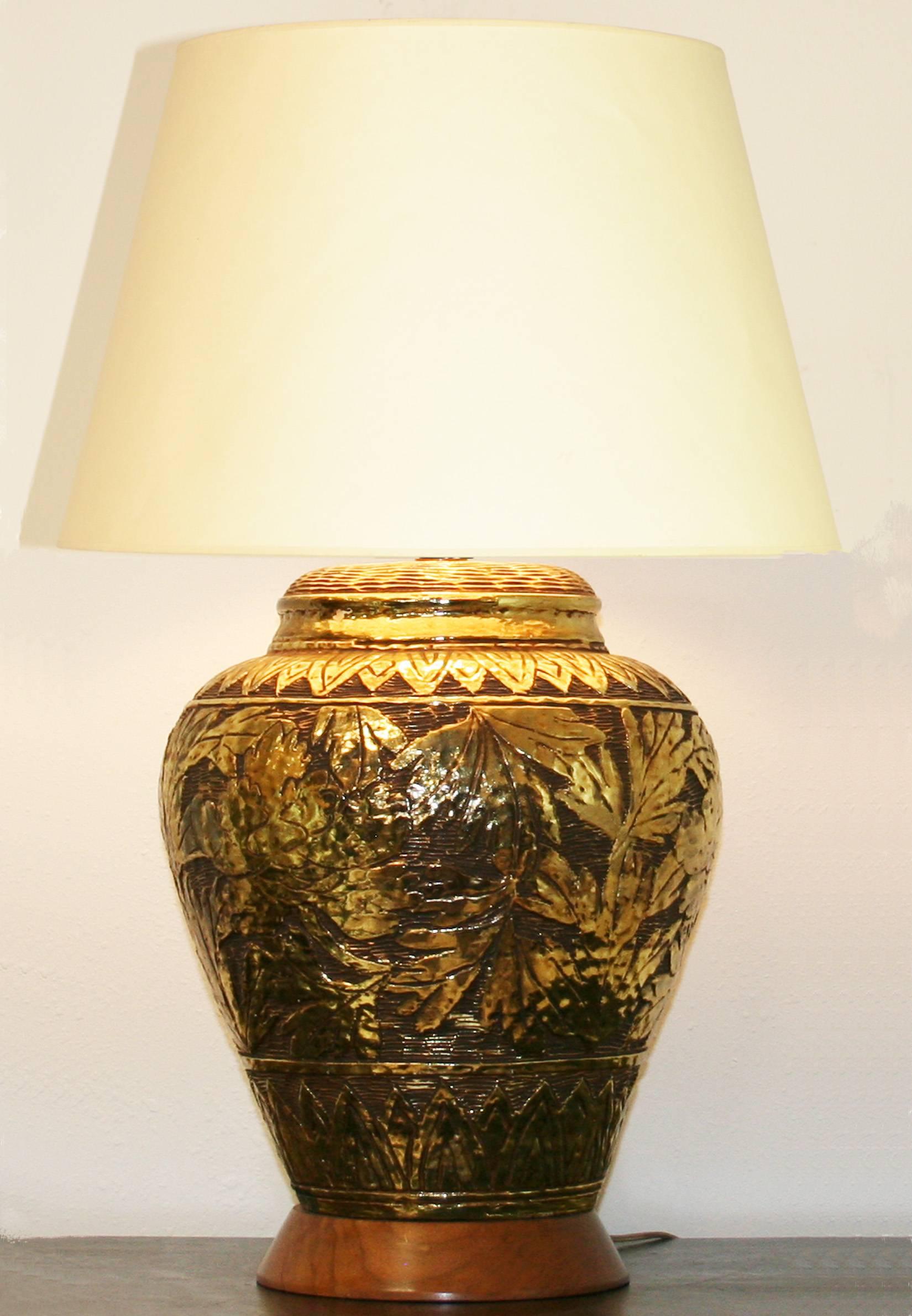 A large gold glazed ceramic lamp with stylized leaf patterns. Shade for display only.