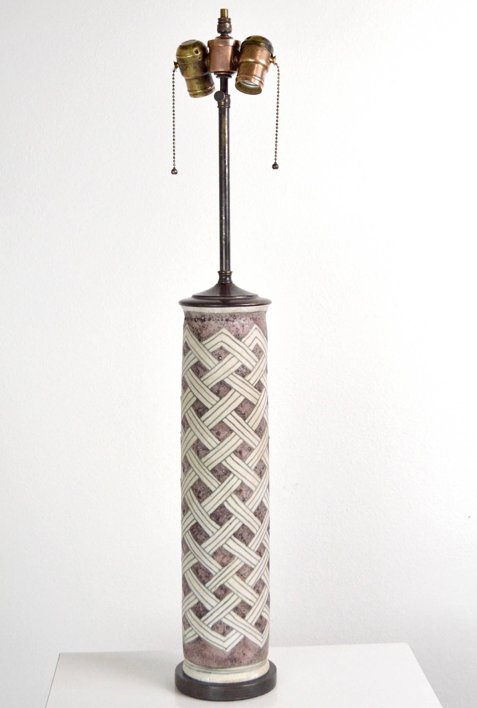 A pair of signed Guido Gambone lamps in a lovely amethyst brown and ivory glaze. Tall cylinders with a trellis pattern are mounted on ribbed antiqued brass bases with new double cluster sockets. Signed with donkey cipher, base only, 18” H x 4"