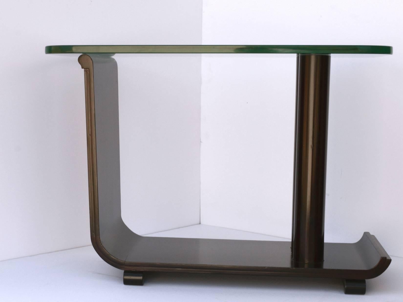 A sculptural side or occasional table in faux grained wood. Shaped columnar support rests on a flat base with stepped edge detail that curves up to support the glass top. The base rests on rounded feet. Original glass top, 1" thick, with age