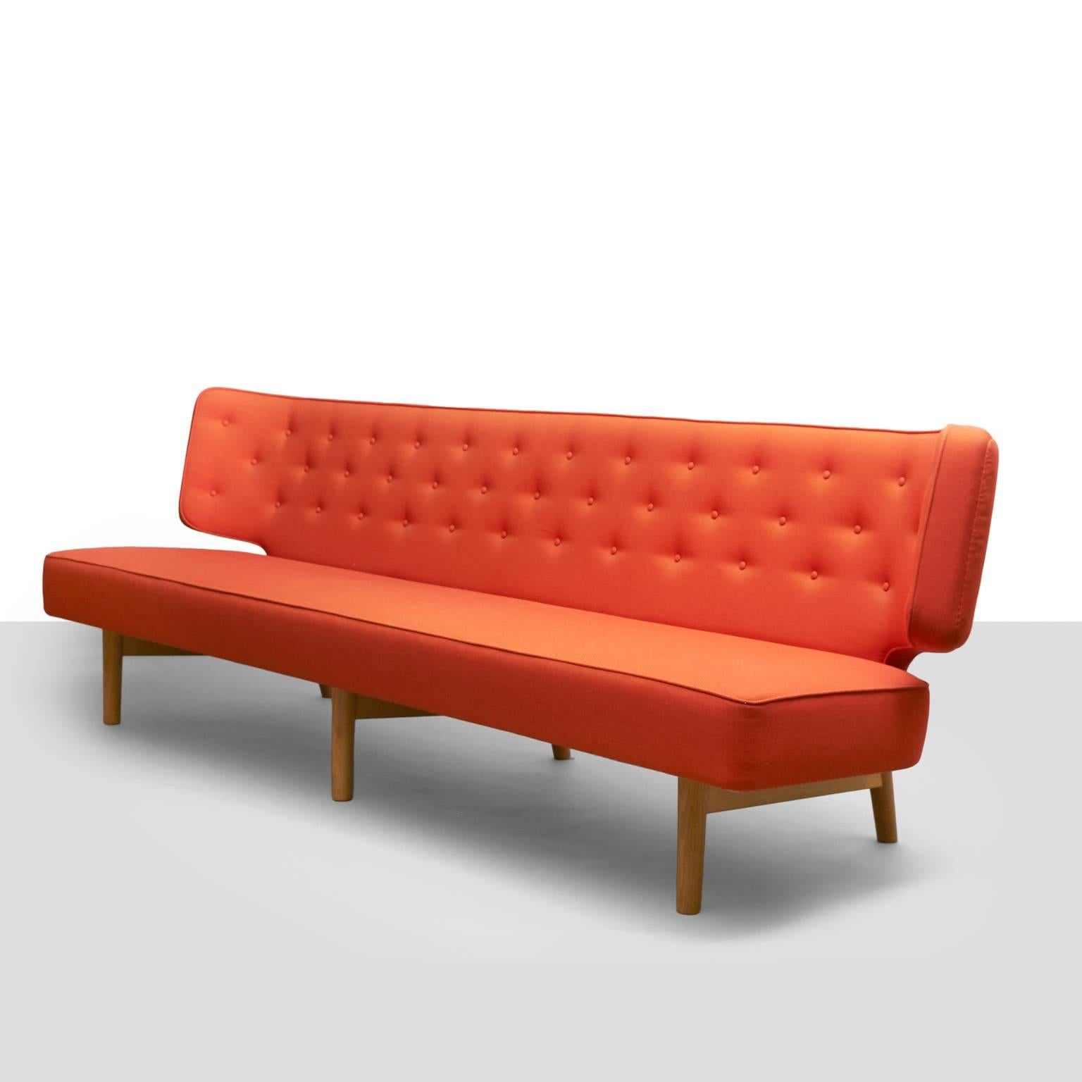 A 3 seat Radiohus Sofa designed by Vilhelm Lauritzen for Brothers Pedersen. A long and sleek, tufted, wing back sofa with beech feet and deep orange upholstery. Designed in 1936 for the Royal Danish Academy of Music, this particular sofa was