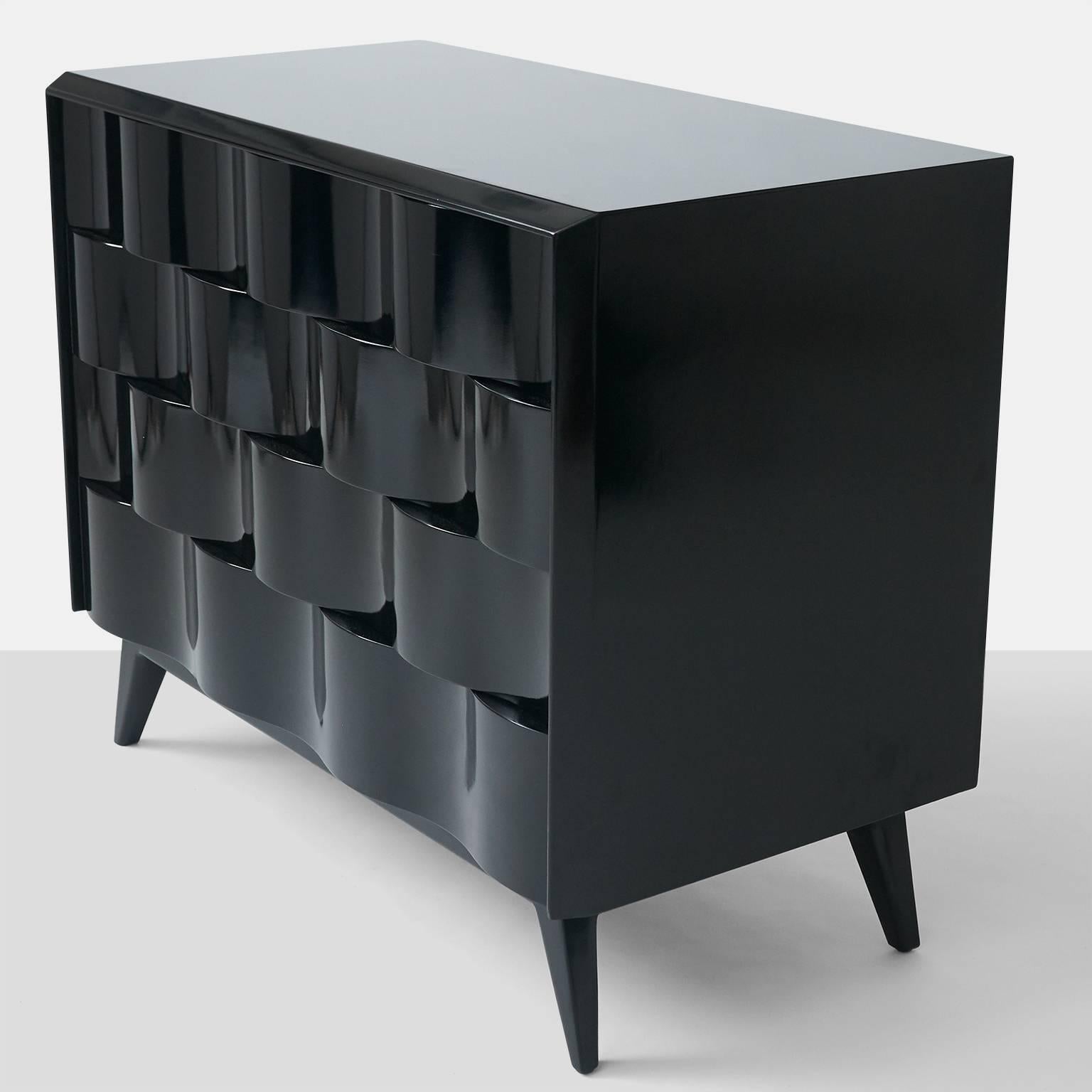 A sculptural wave front four drawer chest beautifully restored in black lacquer with maple drawer interiors. A pair is available.