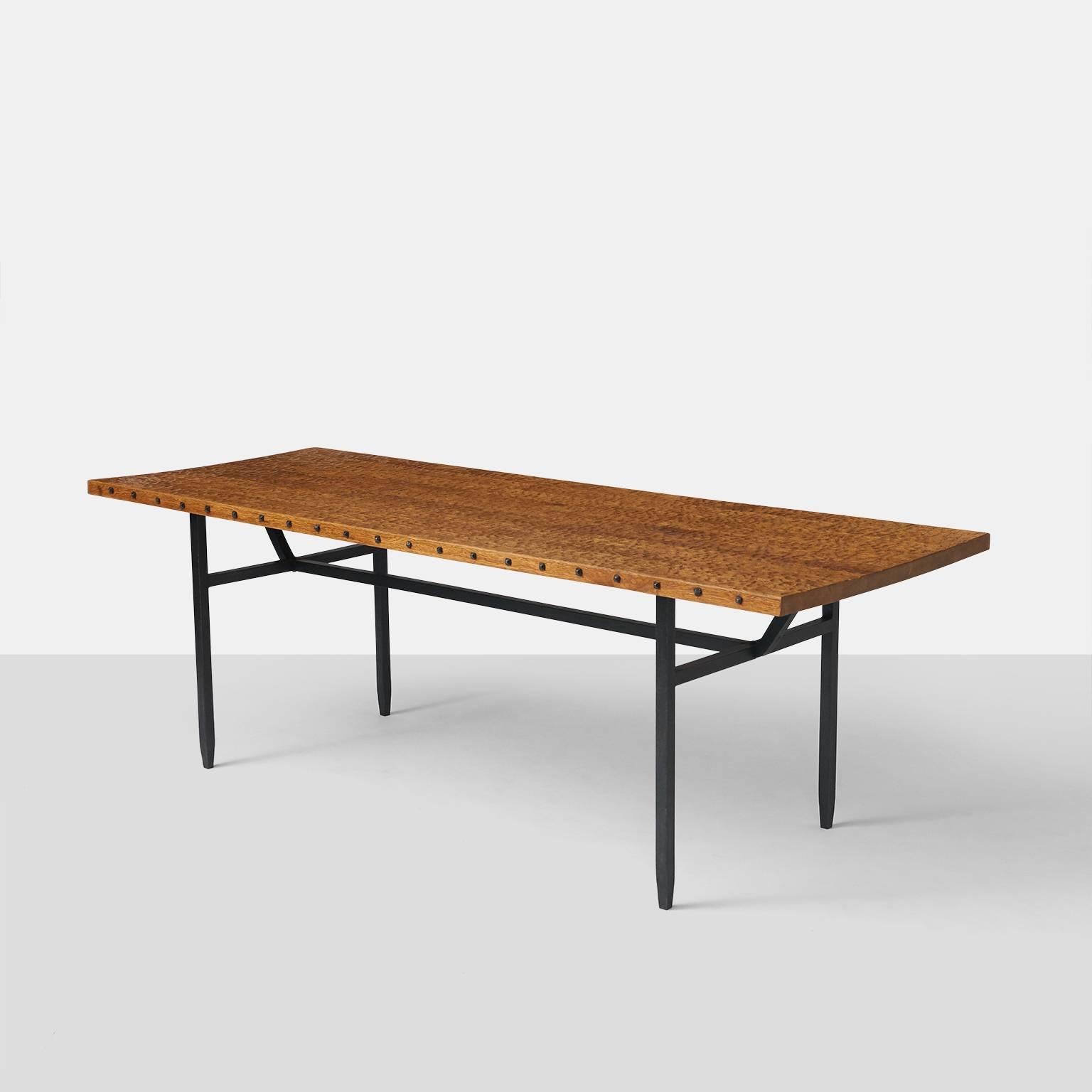 A rectangular dining table by Jean Touret with a hand scraped solid oak top. The edges of the table top are bordered with square form iron nails and a black lacquered iron base with tapered leg ends.  Jean Touret was the designer for the alter at
