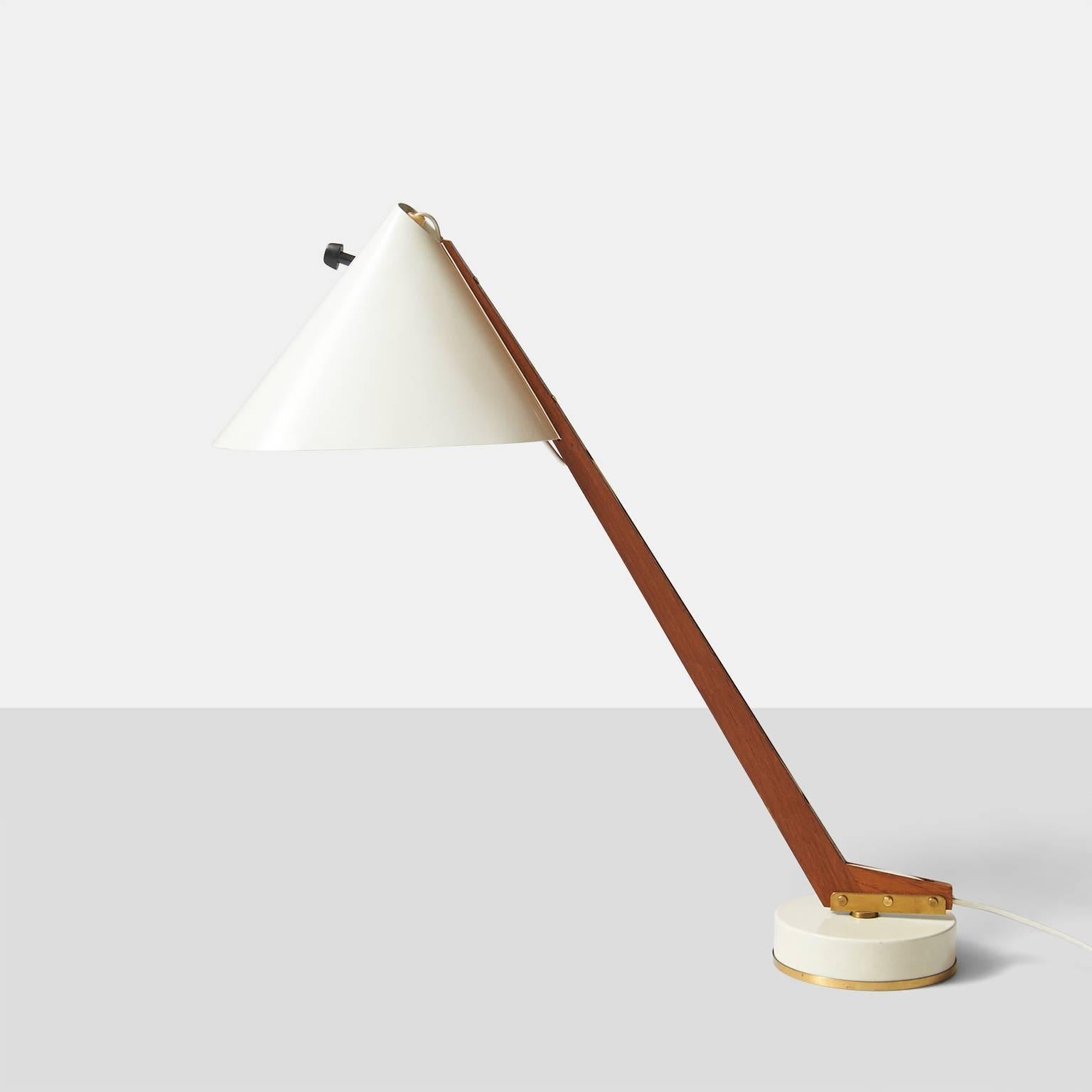 A published desk lamp model B54 by Swedish designer Hans-Agne Jakobsson. White metal base and shade with brass trim and a rotating teak stem. The cord is exposed and recessed into the wood stem. The lamp retains the original label H-A Jakobsson
