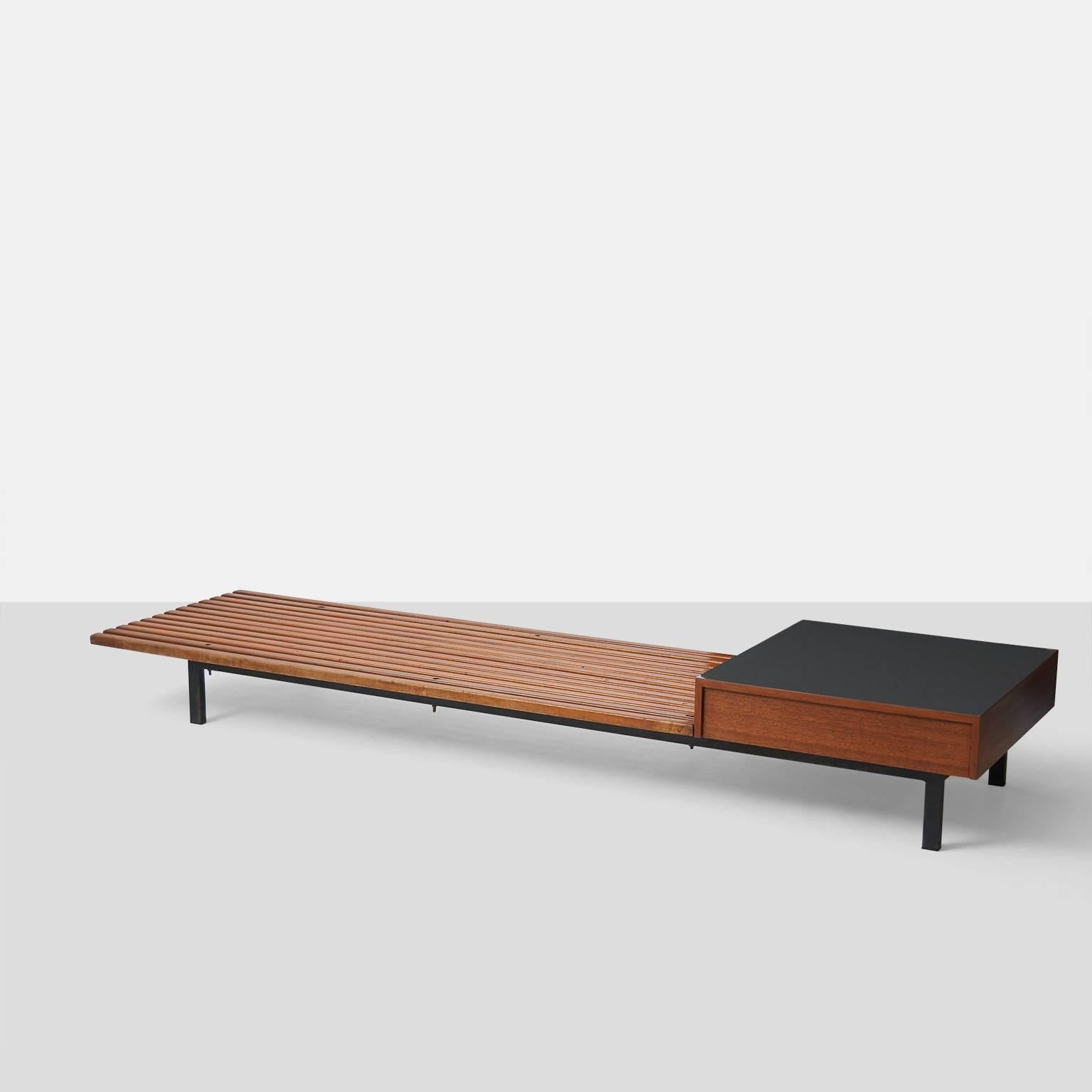 A mahogany slat bench with a side table and drawer from Cite Cansado in Mauritania, 1958. The bench has a steel frame and a drawer that is covered in a gray laminate. Provenance is available.