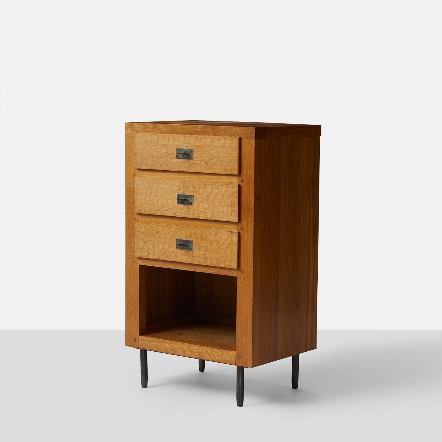 A cupboard by Jean Touret for Atelier Marolles in a natural aged oak finish. The cabinet has three drawers with hand-carved detail, iron pulls and standing on iron legs. Retains the original branding 