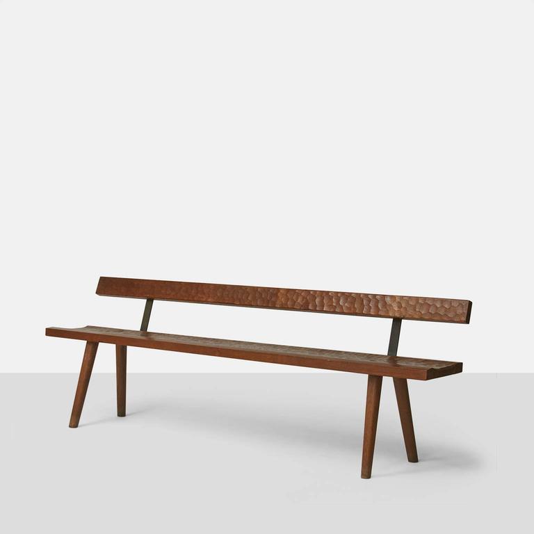 A bench with backrest in a rich aged oak by Jean Touret made with iron connections. The seat and back have the typical hand-carved detail that Touret is known for and there are four tapered legs.