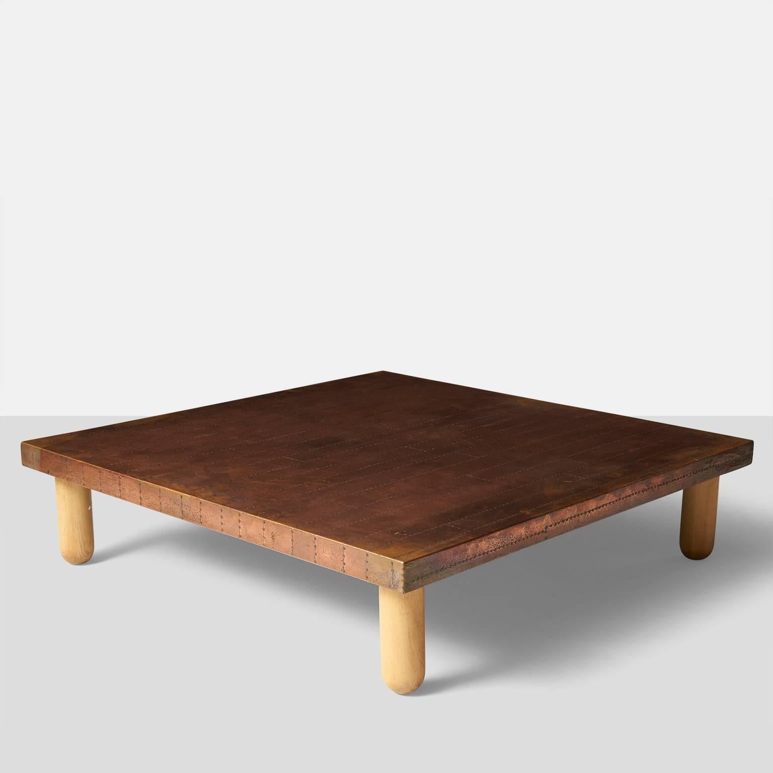 A large coffee table covered and with sheets of patinated copper attached with nail trim in a random plank pattern. Four beech wood legs and retaining the original signature 