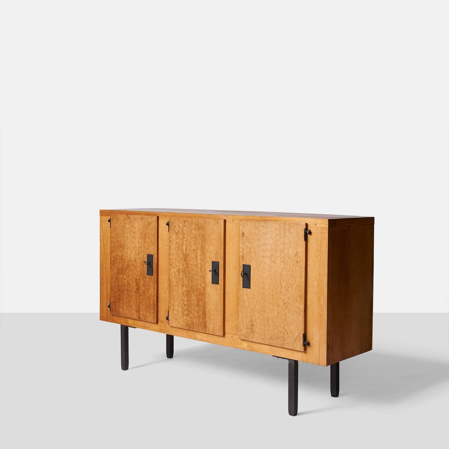 A Jean Touret sideboard with iron legs, hinges and escutcheon with key. There are three doors all with hand-carved detail, two adjustable shelves behind the two right sections and one behind the left side. Exposed dowel construction adds great